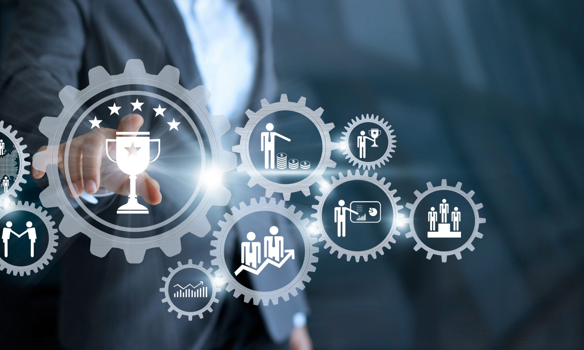 A businessman touches a digital interface of interconnected gears with icons representing success, teamwork, financial growth, and recognition.