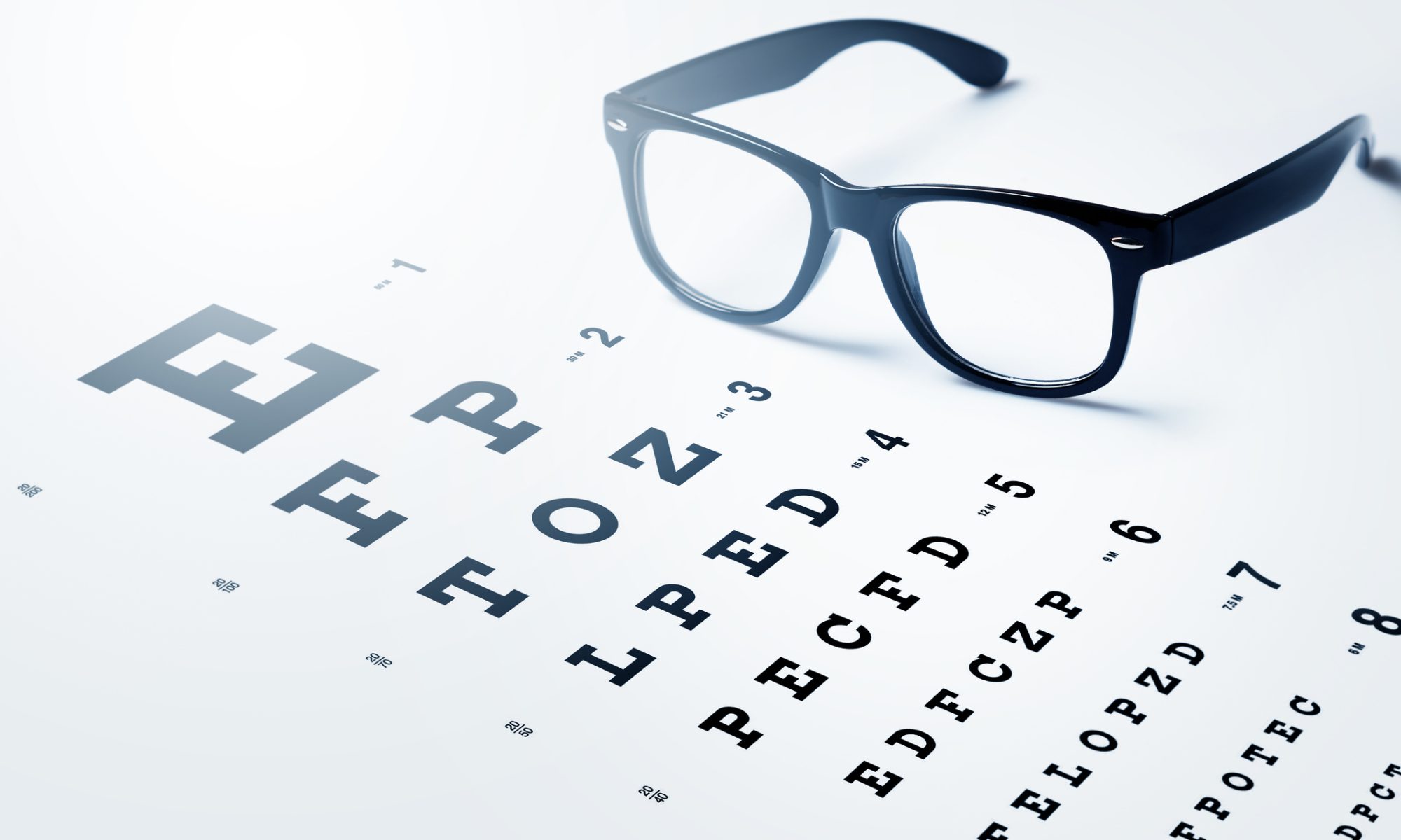 Black-framed eyeglasses resting on top of a Snellen eye chart, commonly used in vision tests.