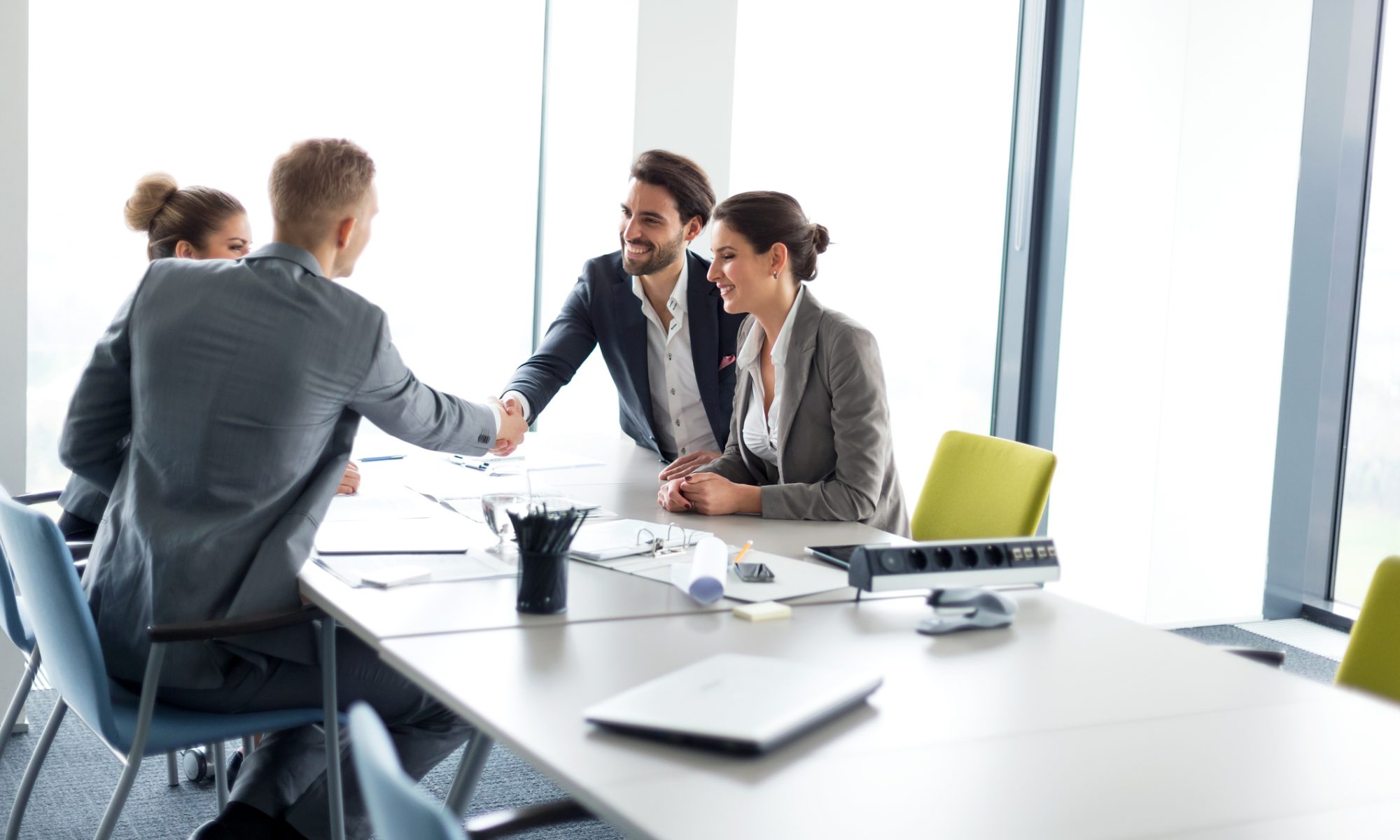 Business executives shaking hands during a meeting, symbolizing a major healthcare acquisition agreement.