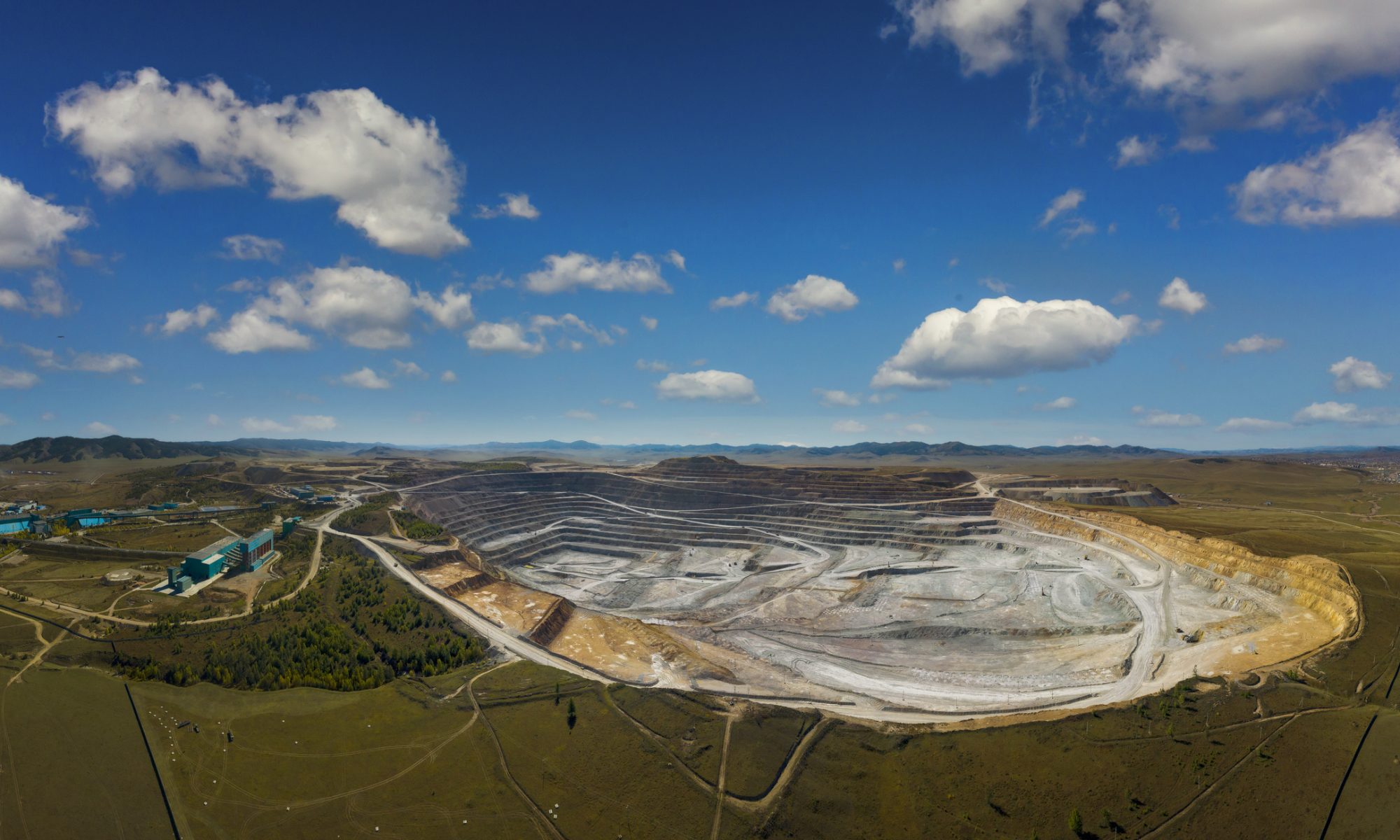 Large open-pit rare earth mining site with terraced excavation and processing facilities visible in the surrounding landscape.