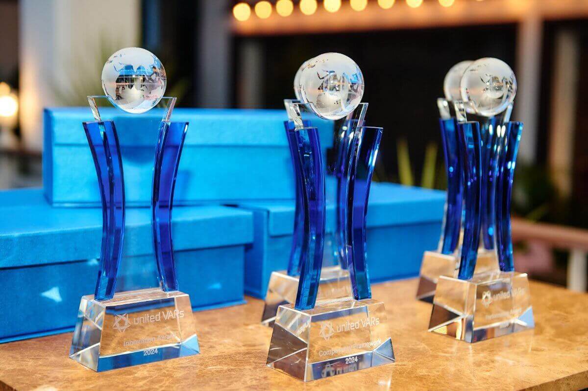Three crystal-and-blue glass award trophies are displayed on a table during an awards ceremony, representing business excellence, global collaboration, and partner recognition.