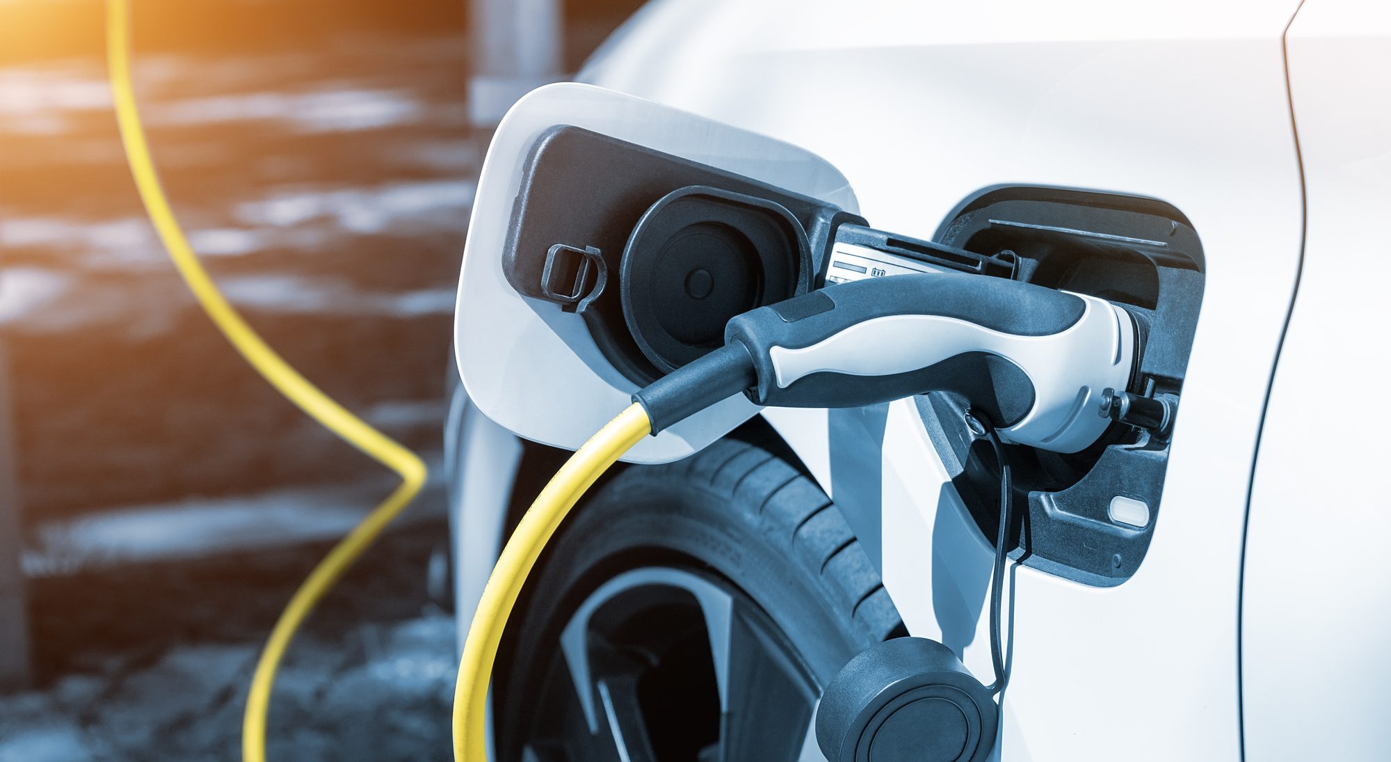 A close-up of an electric vehicle charging cable plugged into a white commercial EV, illustrating fleet electrification and charging infrastructure.