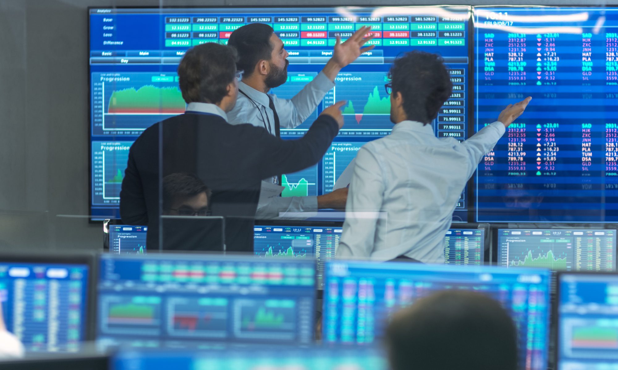 Traders analyze large digital stock market displays showing rising share prices and market data during an active trading session.