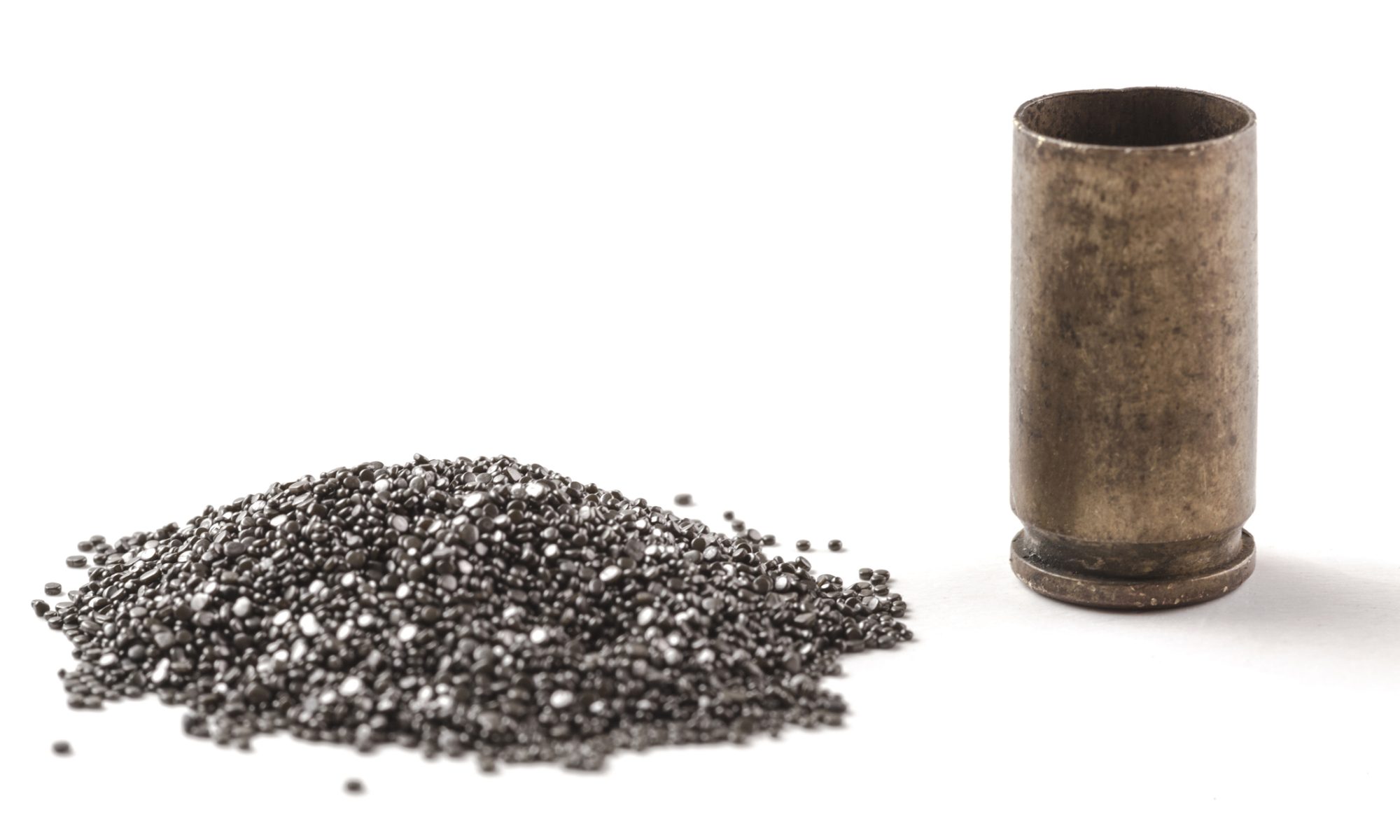 A pile of metallic scandium granules sits beside a metal sample container, representing critical minerals used in aerospace and defense manufacturing.