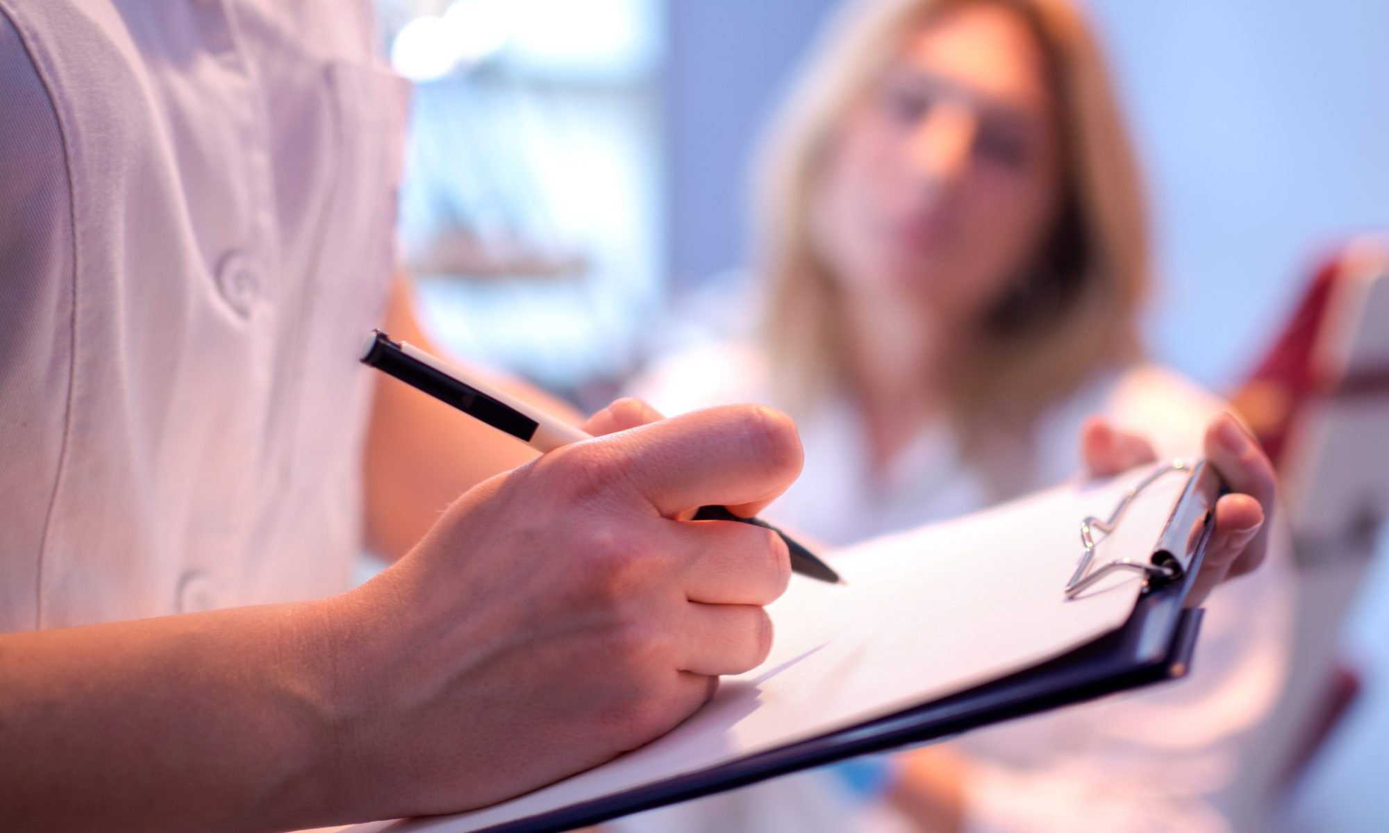 Healthcare professional taking notes on a clipboard while speaking with a patient, representing clinical research and patient testing for alcohol use disorder.