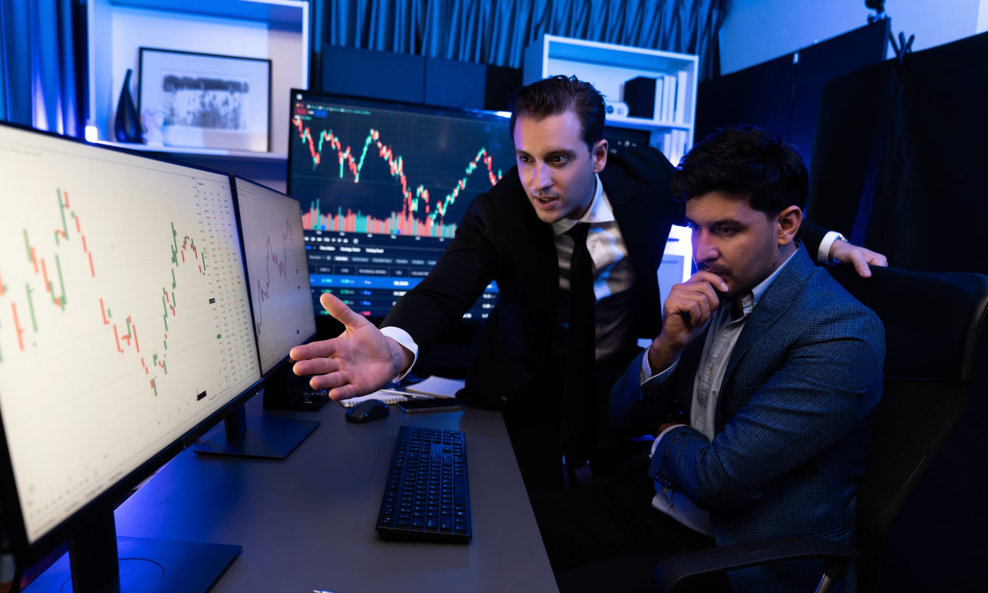 Two market professionals analyze stock charts on multiple monitors as biotech and semiconductor stocks lead PRISM’s mid-day market movers.