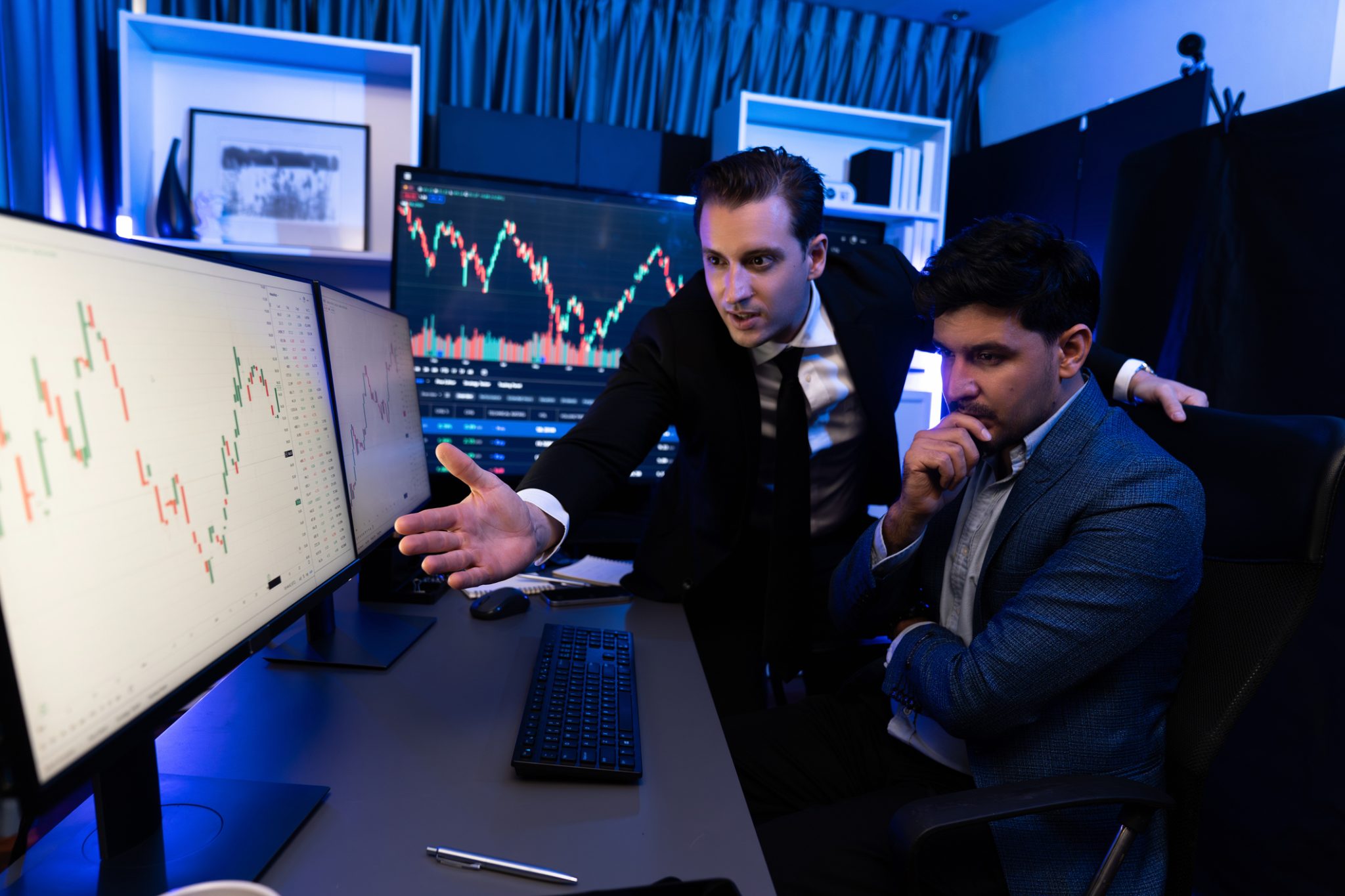 Two market professionals analyze stock charts on multiple monitors as biotech and semiconductor stocks lead PRISM’s mid-day market movers.