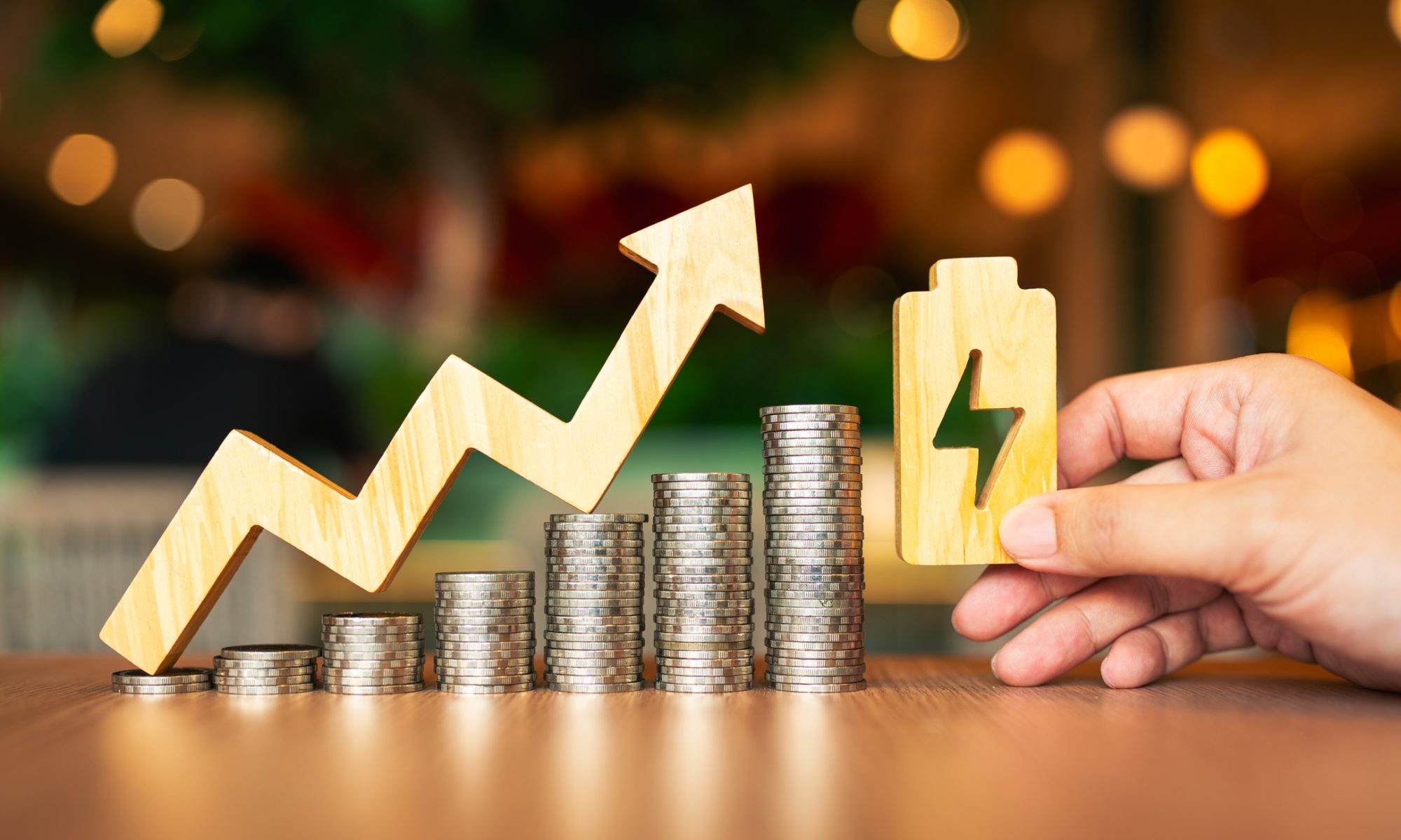 Stacks of coins rising beneath an upward arrow beside a battery symbol, representing American Battery Technology Company’s revenue growth, improving gross profit, and lithium expansion plans.