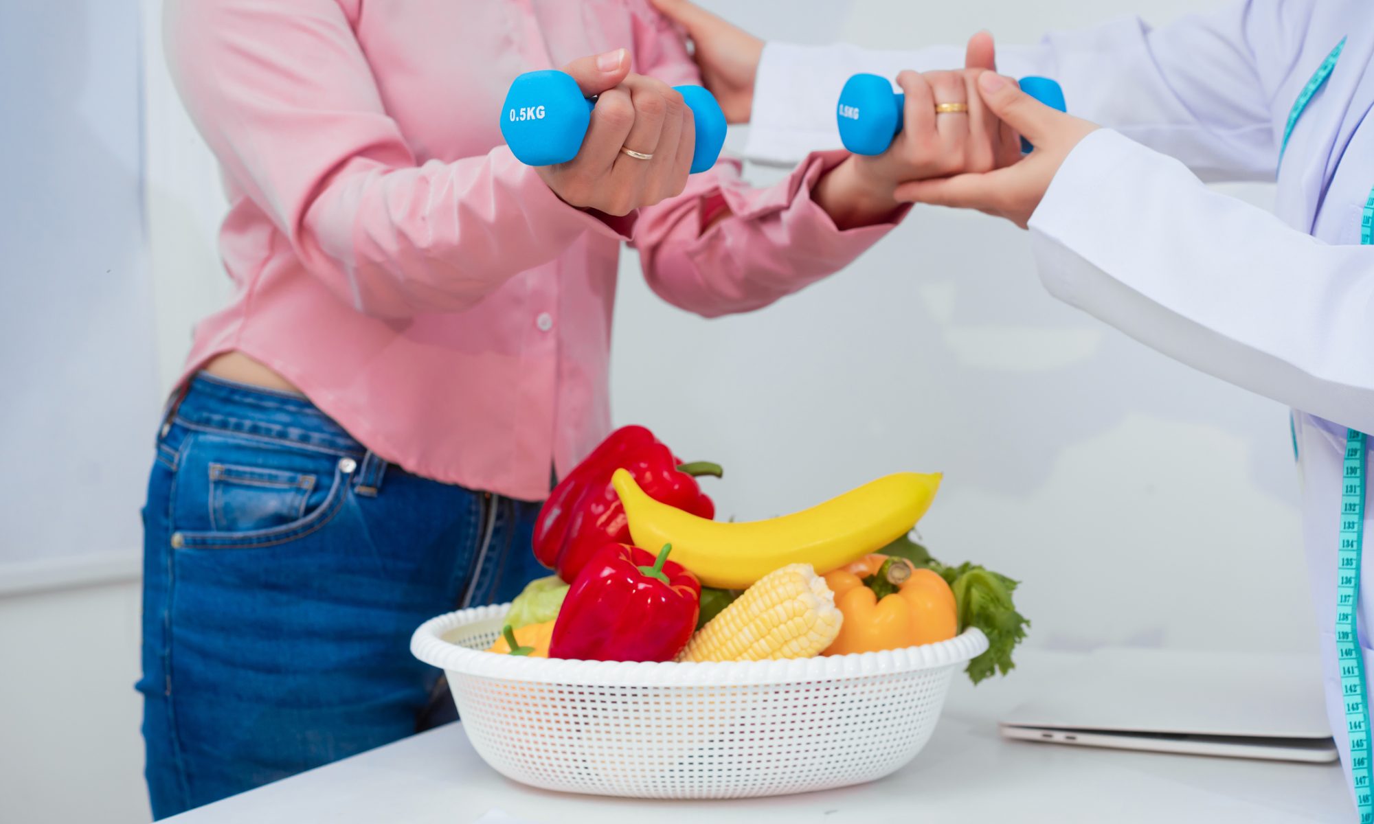 Woman exercising with light dumbbells while receiving guidance from a health professional, with fresh fruits and vegetables nearby, representing nutrition, coaching, fitness, and metabolic health.