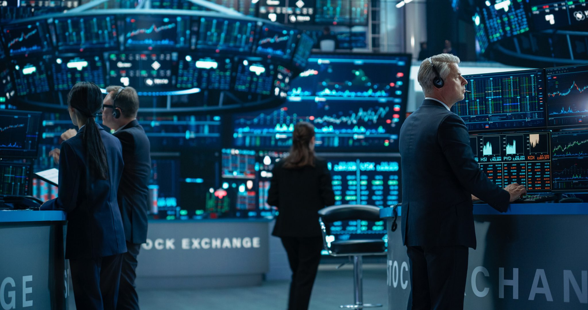 Traders monitor stock charts and market data across multiple screens on a busy exchange floor, representing heavy trading activity in biotech and consumer products stocks.