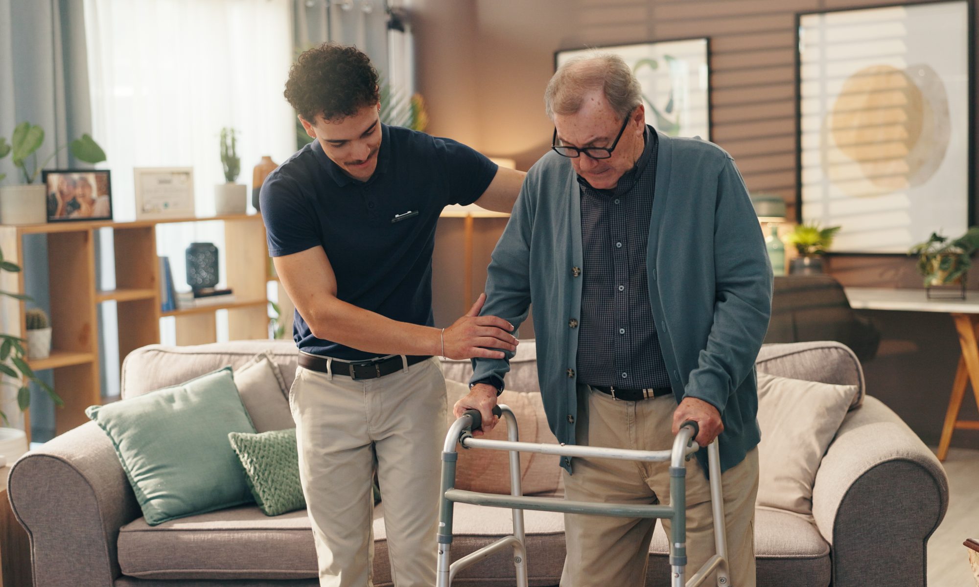 Caregiver assisting an older man using a walker at home, representing support for people living with Parkinson’s disease and mobility challenges.