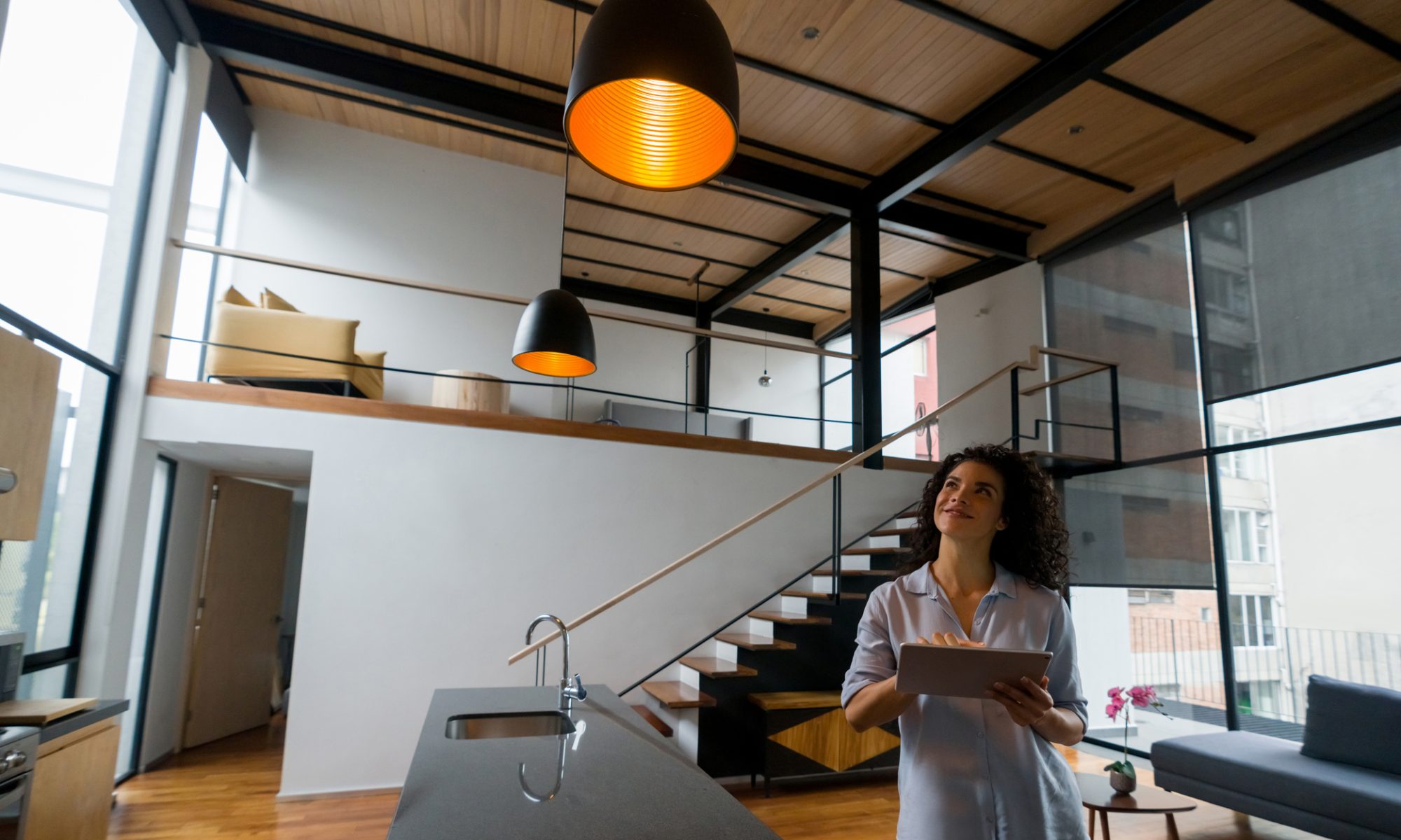 Woman uses a tablet to control lighting in a modern home, representing connected smart-home technology and intelligent electrical systems.