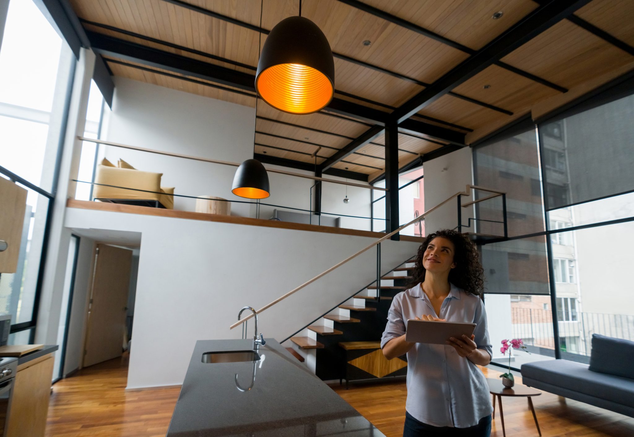 Woman uses a tablet to control lighting in a modern home, representing connected smart-home technology and intelligent electrical systems.