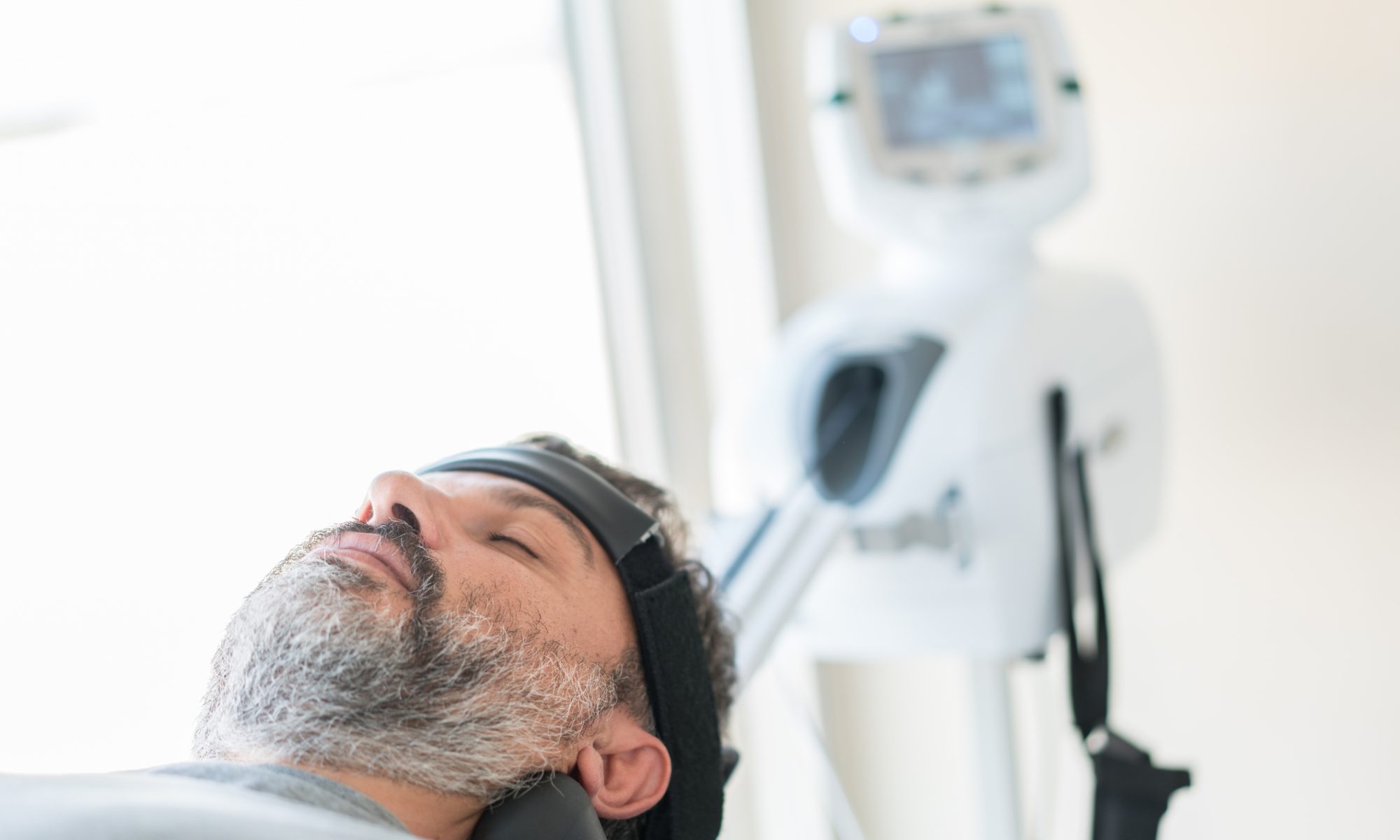 Patient undergoes transcranial magnetic stimulation treatment using a medical device, representing robotic TMS technology for psychiatric care.