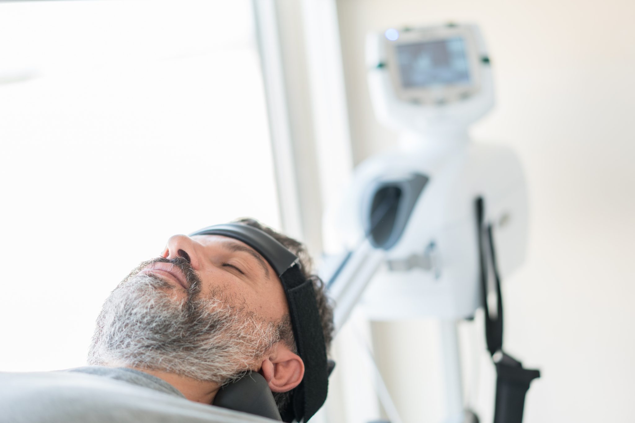 Patient undergoes transcranial magnetic stimulation treatment using a medical device, representing robotic TMS technology for psychiatric care.