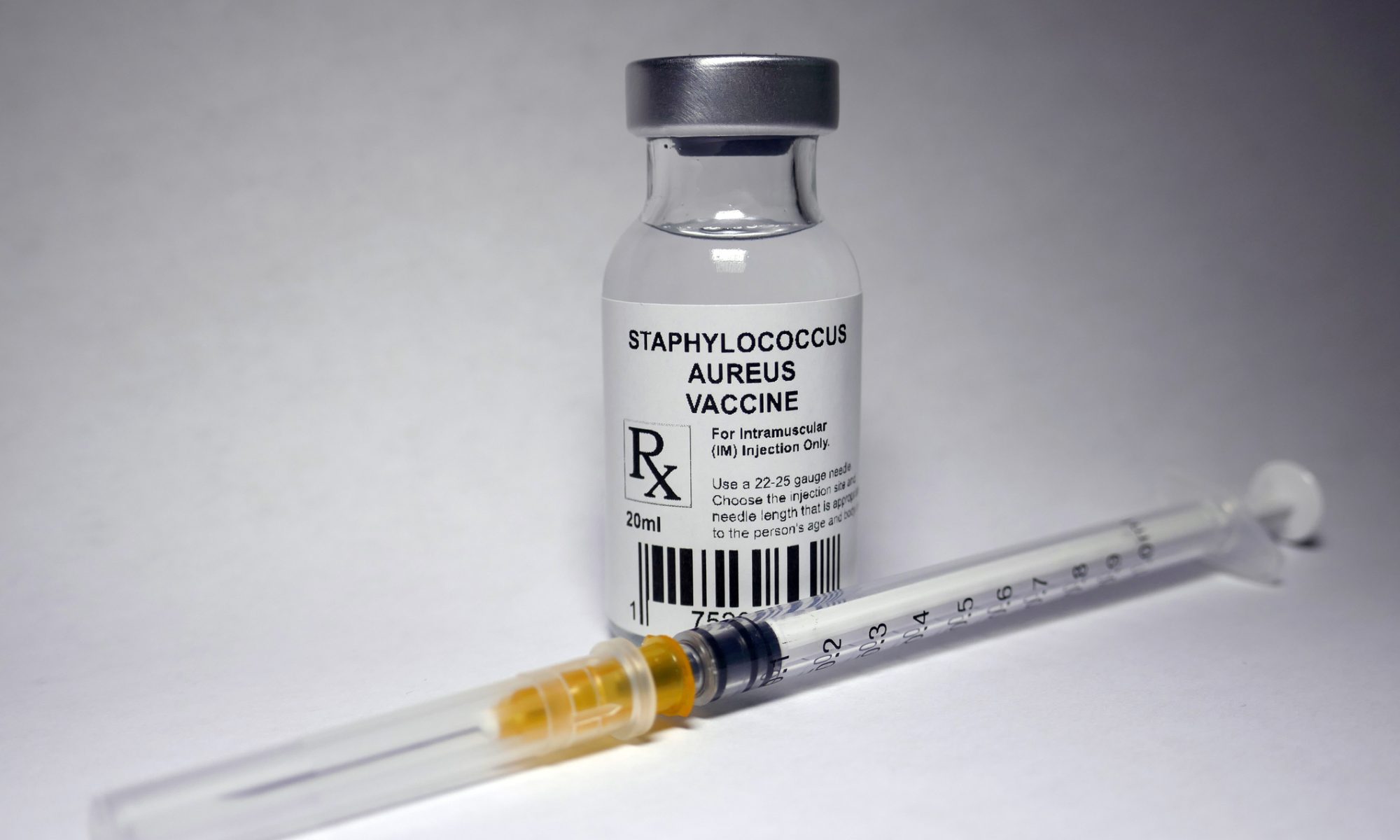 Vial labeled for Staphylococcus aureus beside a syringe, illustrating research into treatments for serious staph infections.