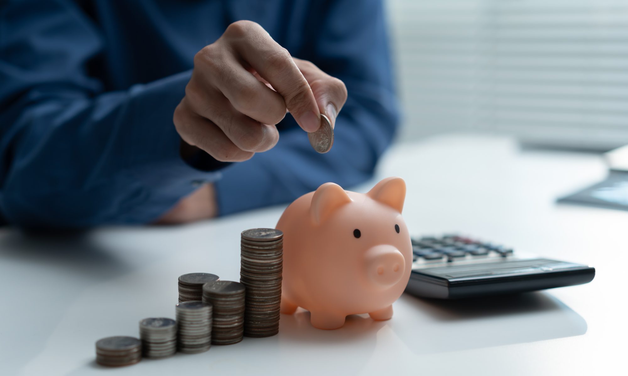 Person placing a coin into a piggy bank beside growing stacks of coins and a calculator, representing DeFi Development’s expanding Solana treasury.