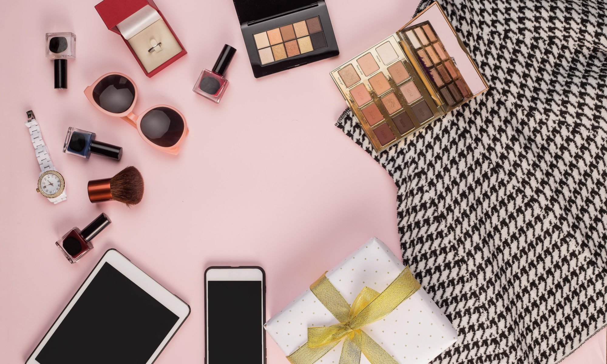 Beauty, fashion and lifestyle accessories arranged on a pink background, representing the new digital-first venture from Donatella Versace and REVOLVE.