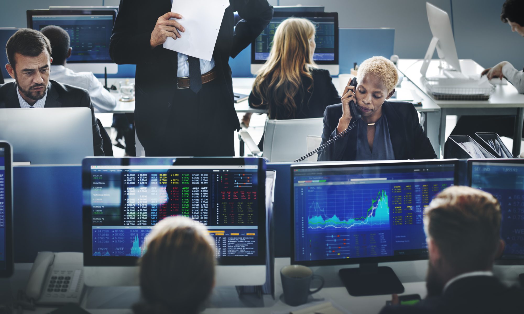 Financial professionals monitor market data and stock charts across multiple computer screens on a busy trading floor, representing active trading in weight-loss and pet-care stocks.