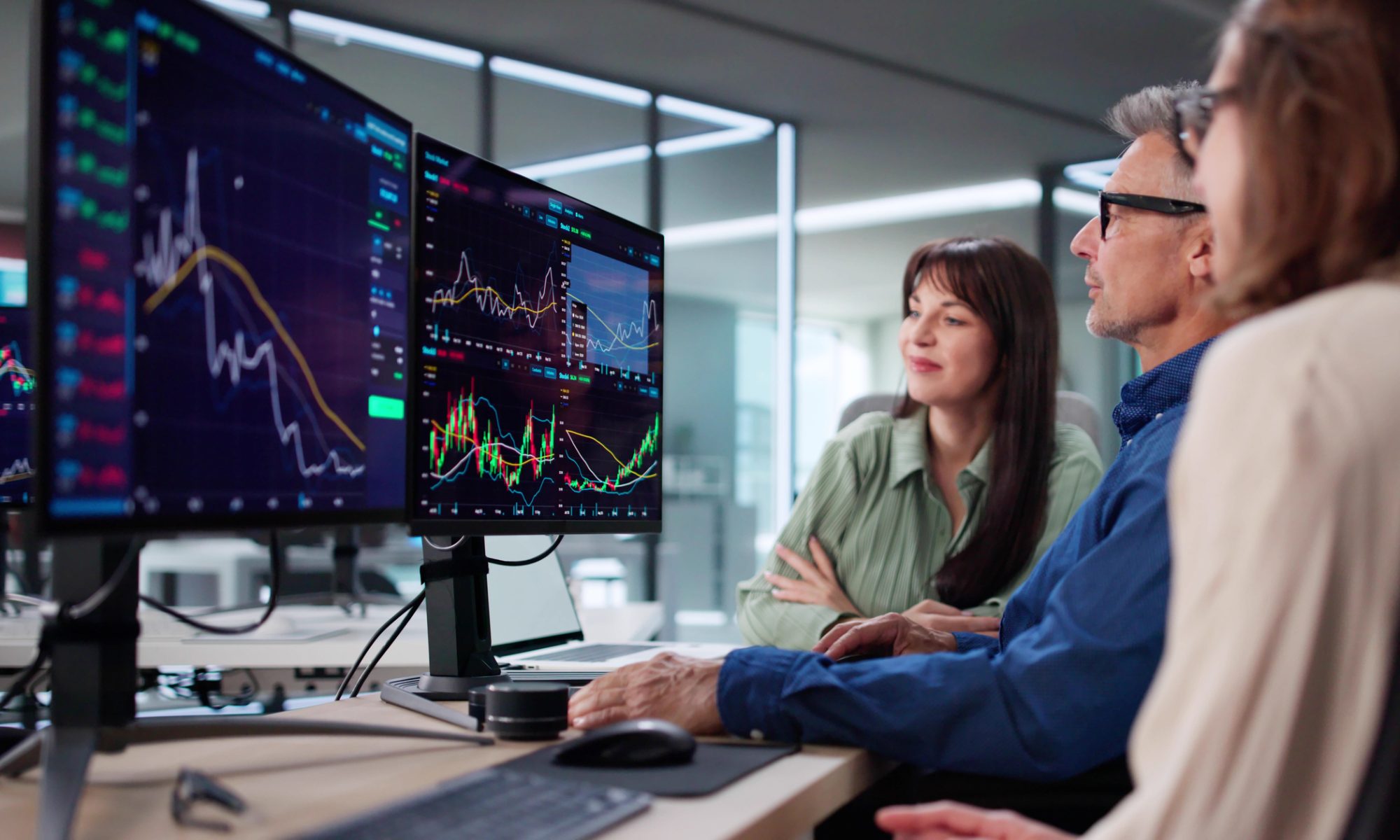 Financial professionals review stock-market charts across multiple monitors, representing active trading and mid-day market movers.