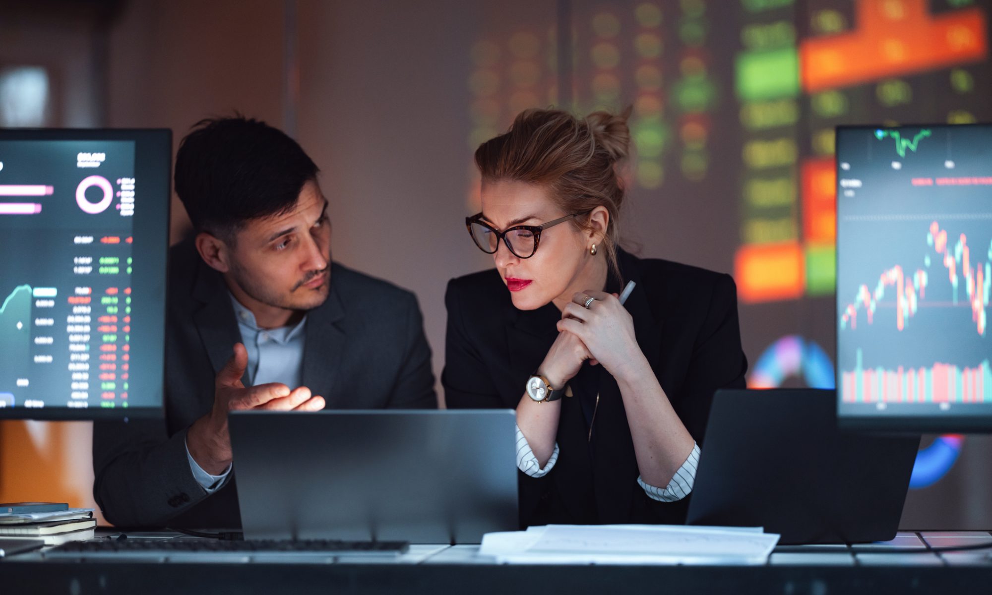 Financial professionals analyze stock-market charts and trading data on multiple screens, representing heavy trading activity in cybersecurity and MedTech stocks.