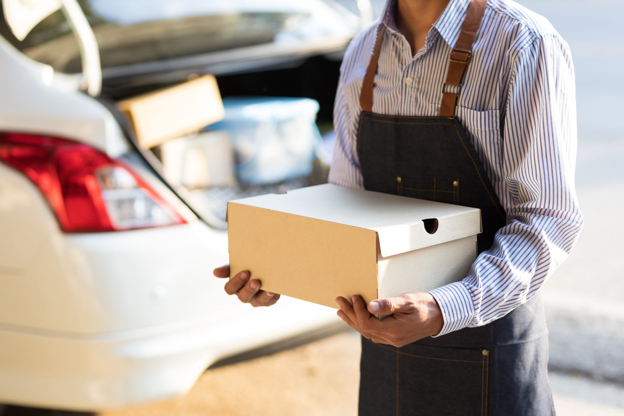 Catering worker carries a food delivery box beside a vehicle, representing workplace catering and large-order food delivery.