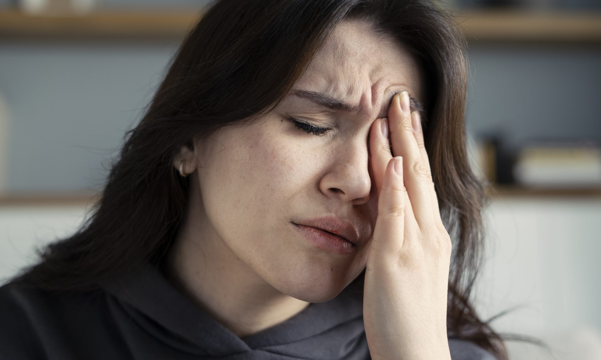 Woman experiencing eye pain holds her hand against her eye, representing neuropathic corneal pain and ocular discomfort.