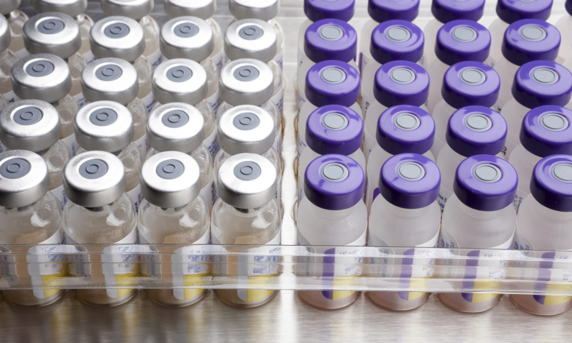 Rows of pharmaceutical vials with silver and purple caps arranged for medical distribution.