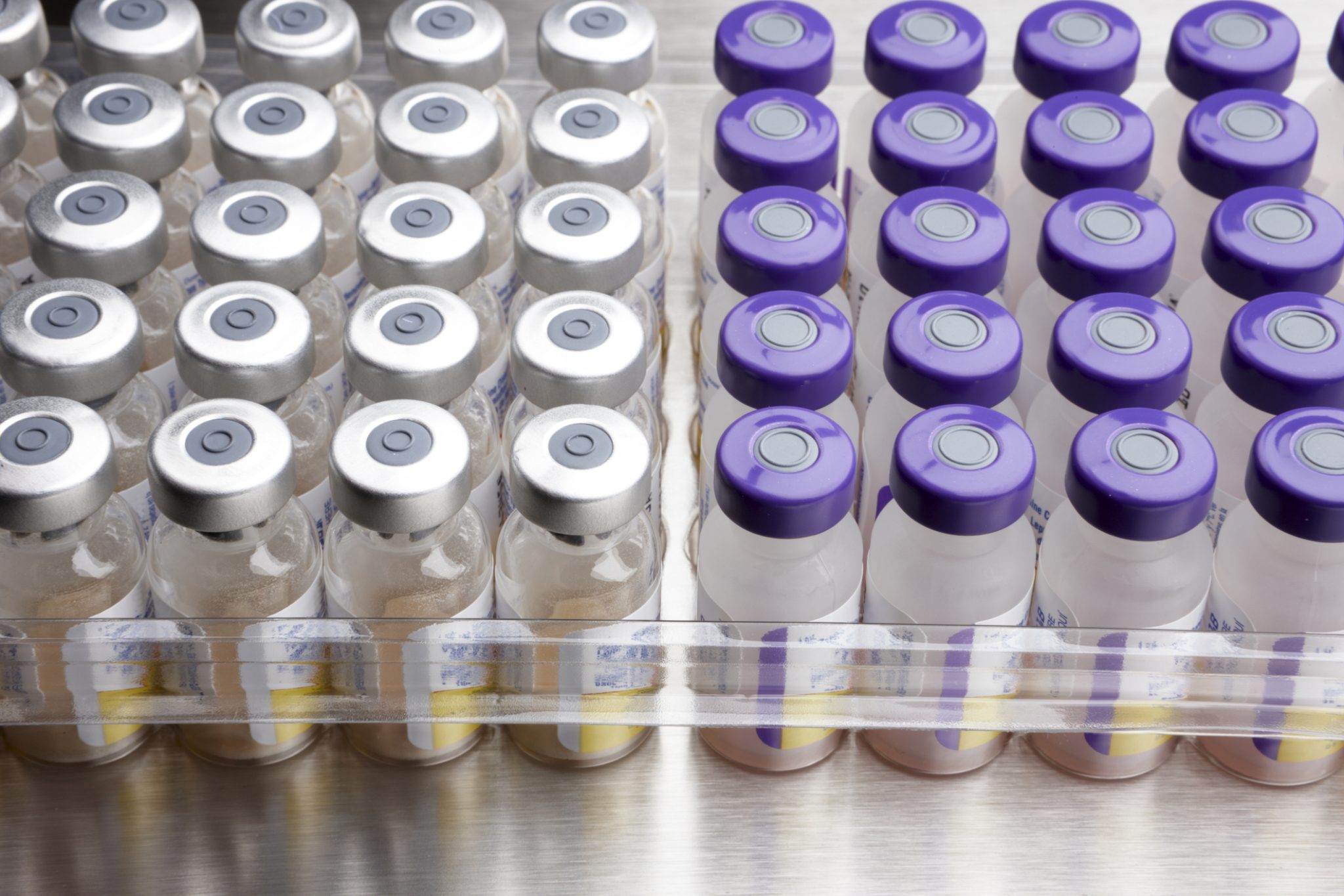 Rows of pharmaceutical vials with silver and purple caps arranged for medical distribution.
