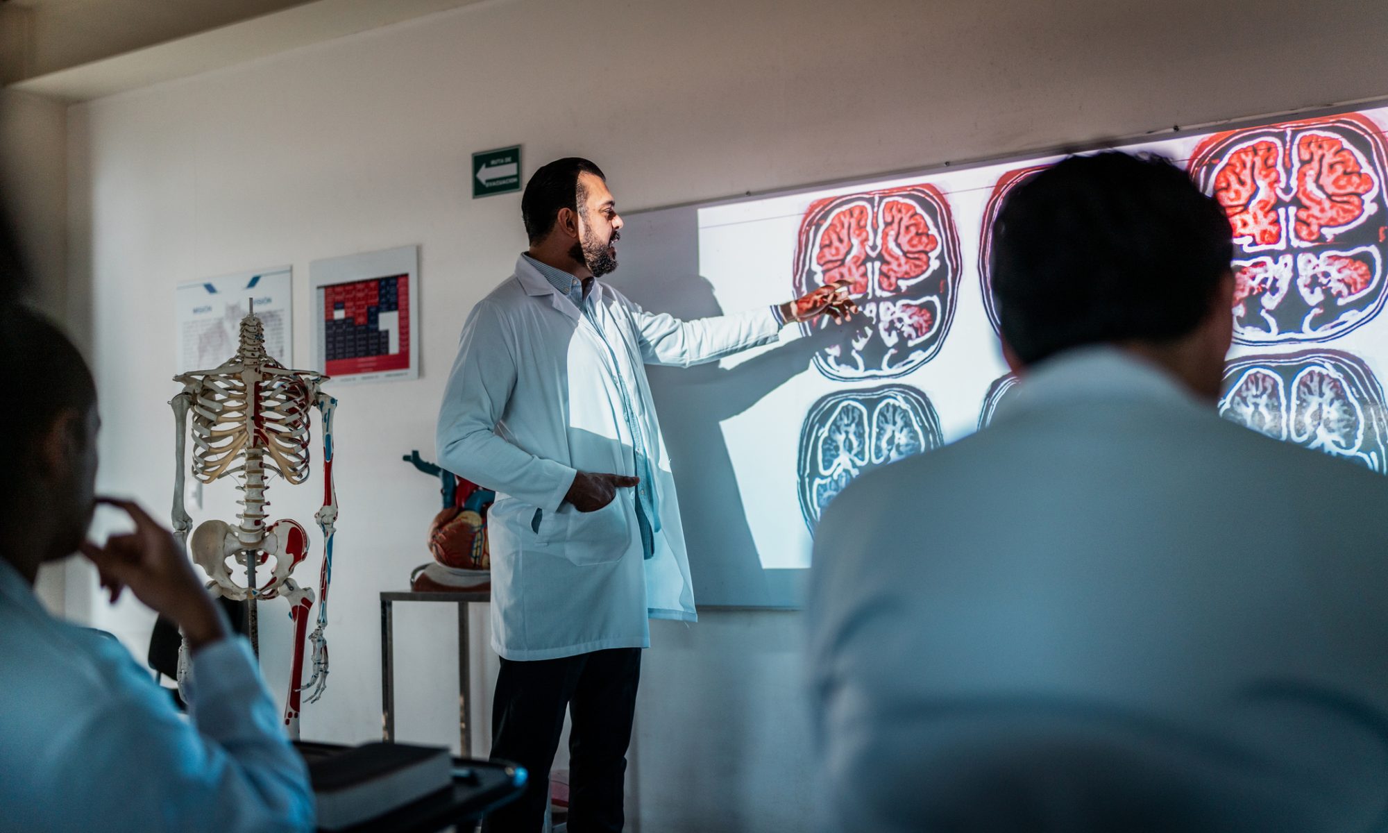 Medical professional presenting brain scans to colleagues in a classroom, illustrating neurological research and advances in glioblastoma treatment.