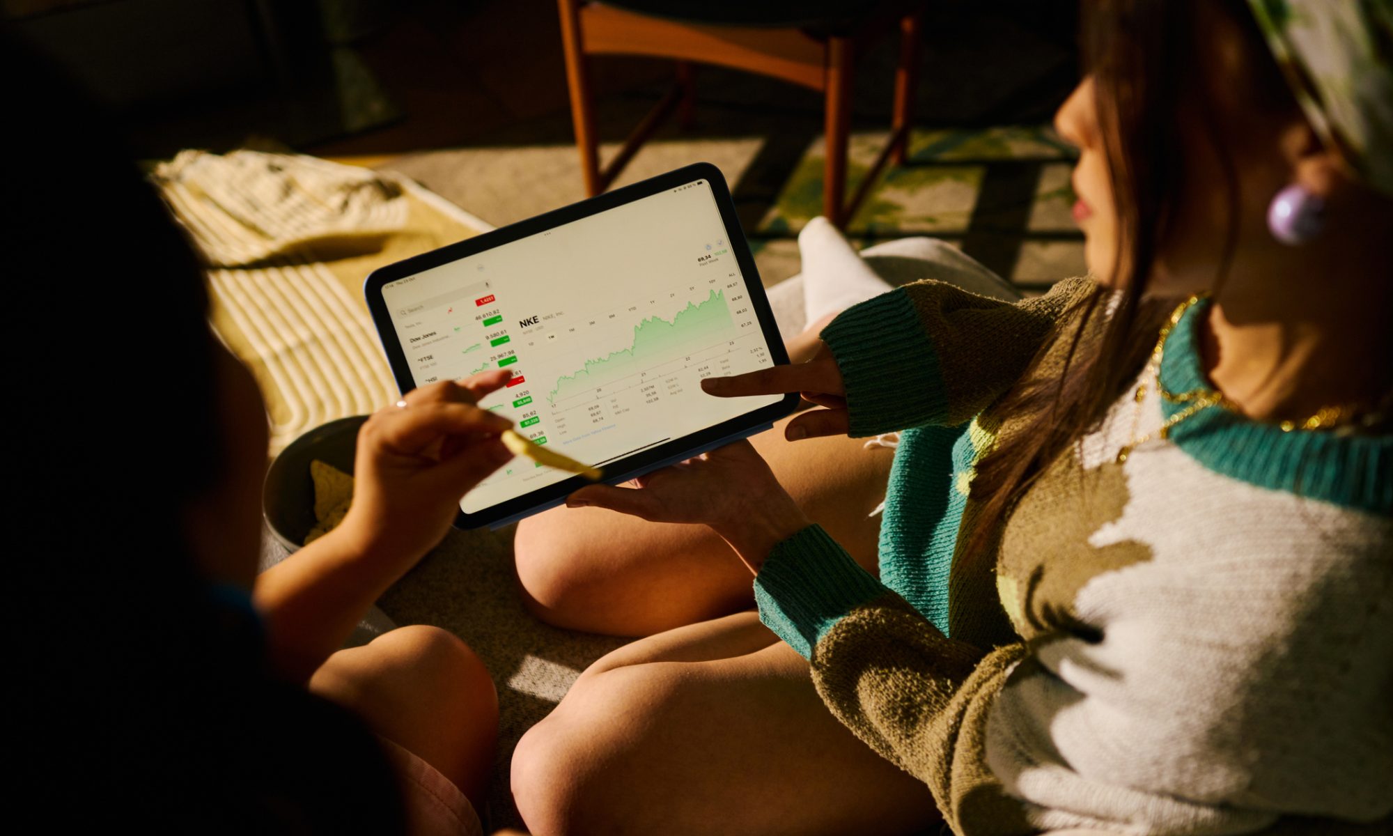 Two people reviewing stock market performance on a tablet displaying financial charts, stock prices, and trading data, representing midday market activity and investment trends.