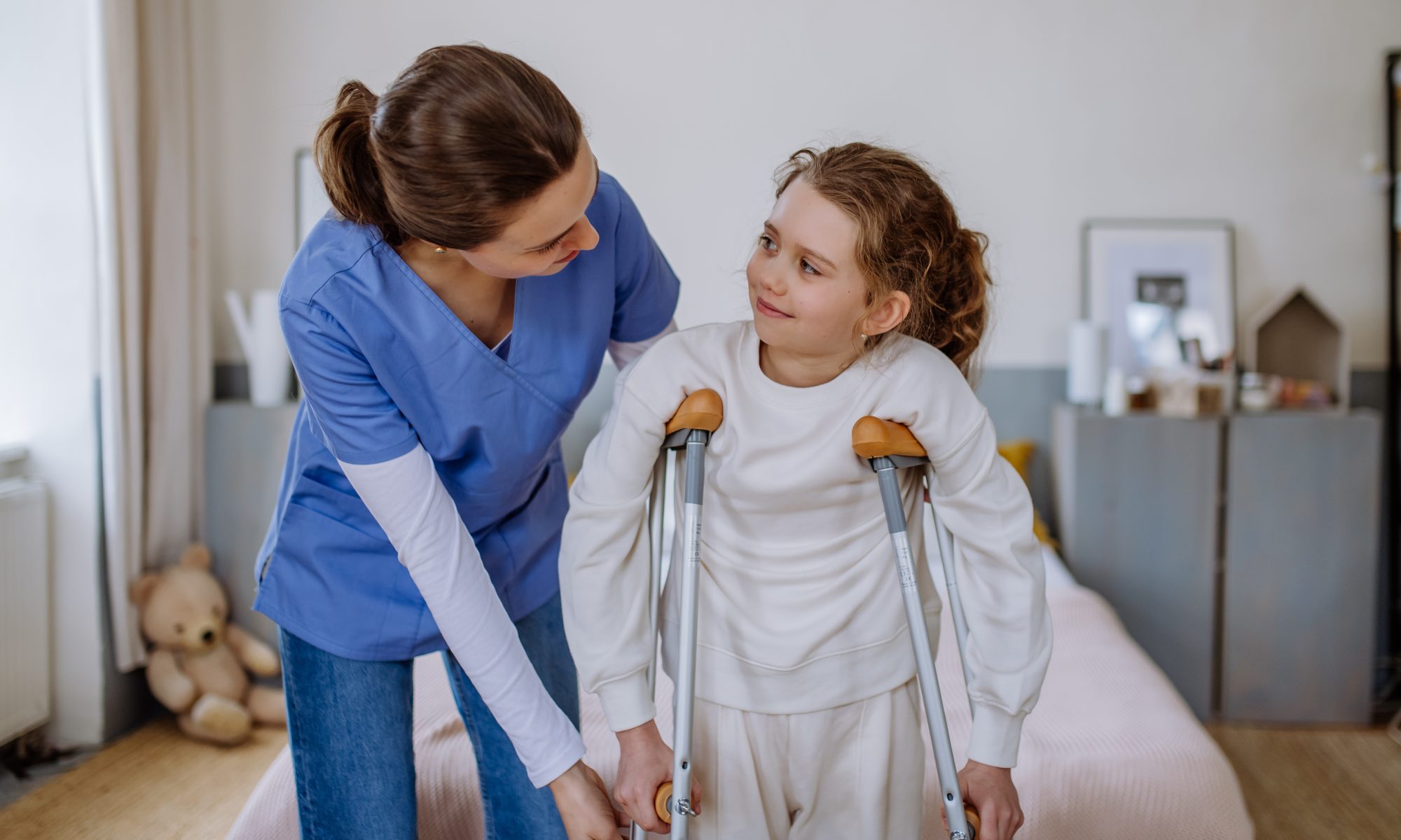 Healthcare professional in blue scrubs assisting a young girl using crutches, illustrating pediatric mobility challenges and treatment needs associated with rare bone diseases.