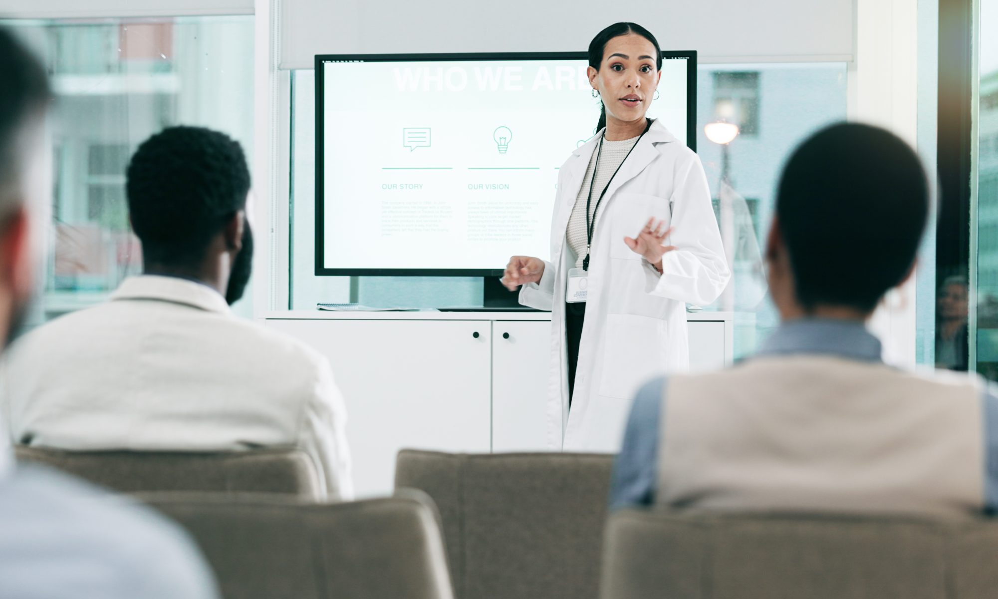 Healthcare professional in a white lab coat presenting medical information to an audience, illustrating clinical research and advances in dialysis access treatments.