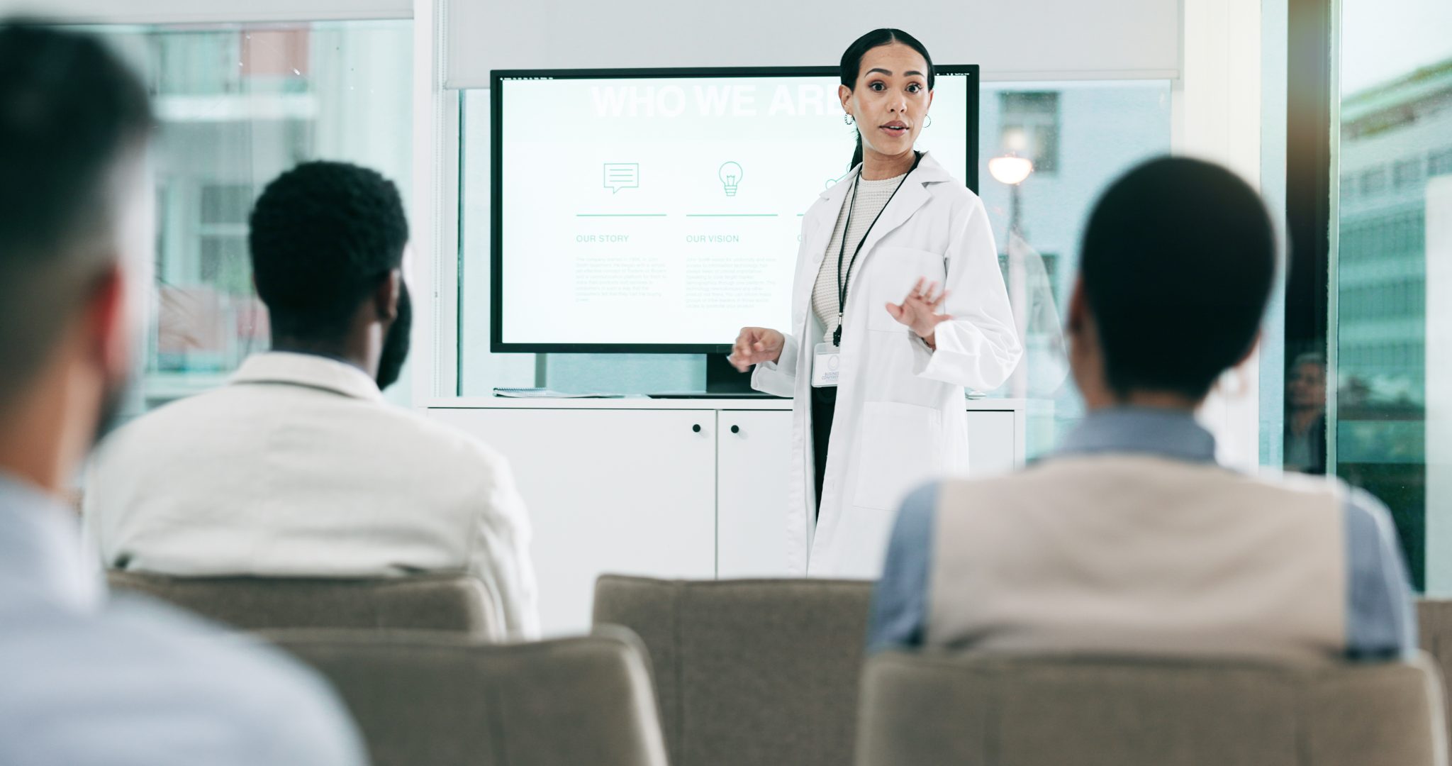 Healthcare professional in a white lab coat presenting medical information to an audience, illustrating clinical research and advances in dialysis access treatments.