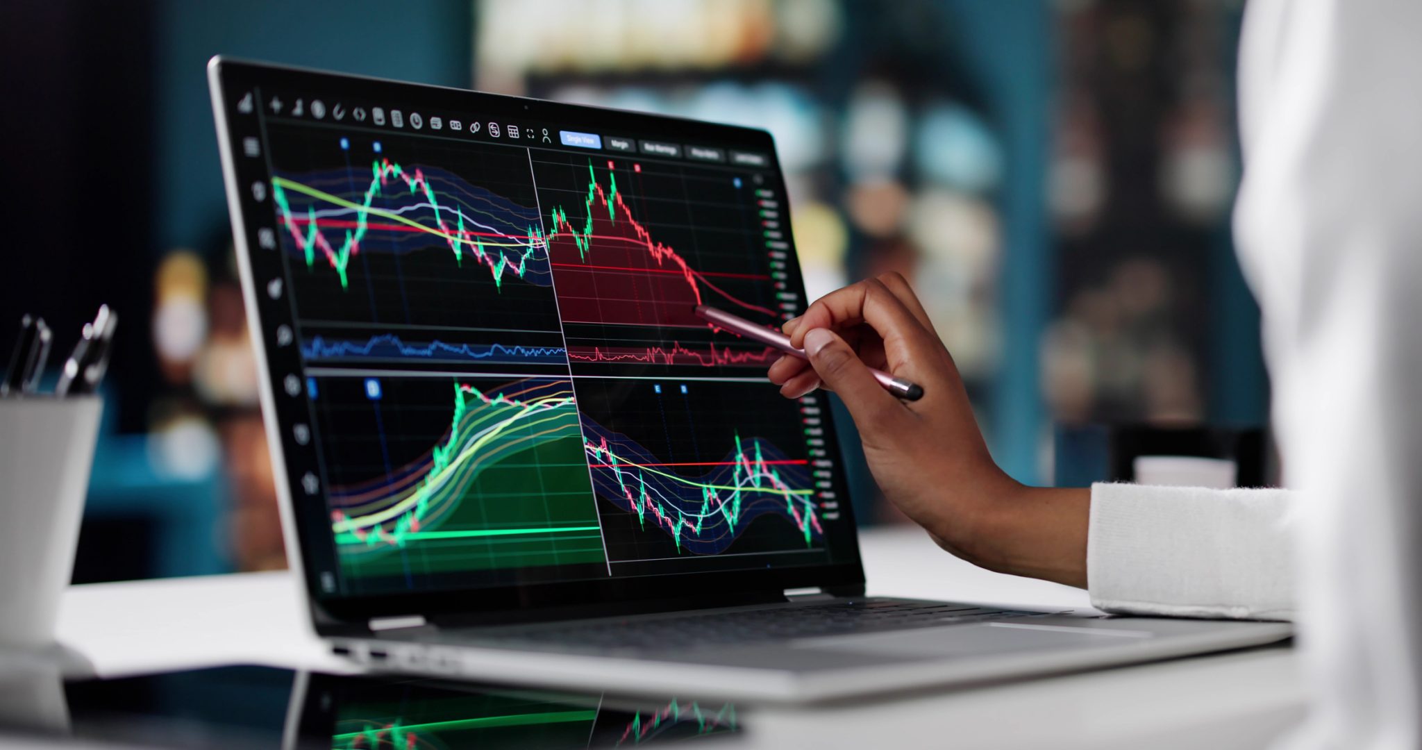 Investor analyzing stock market charts on a laptop, using a stylus to examine trading trends and price movements.