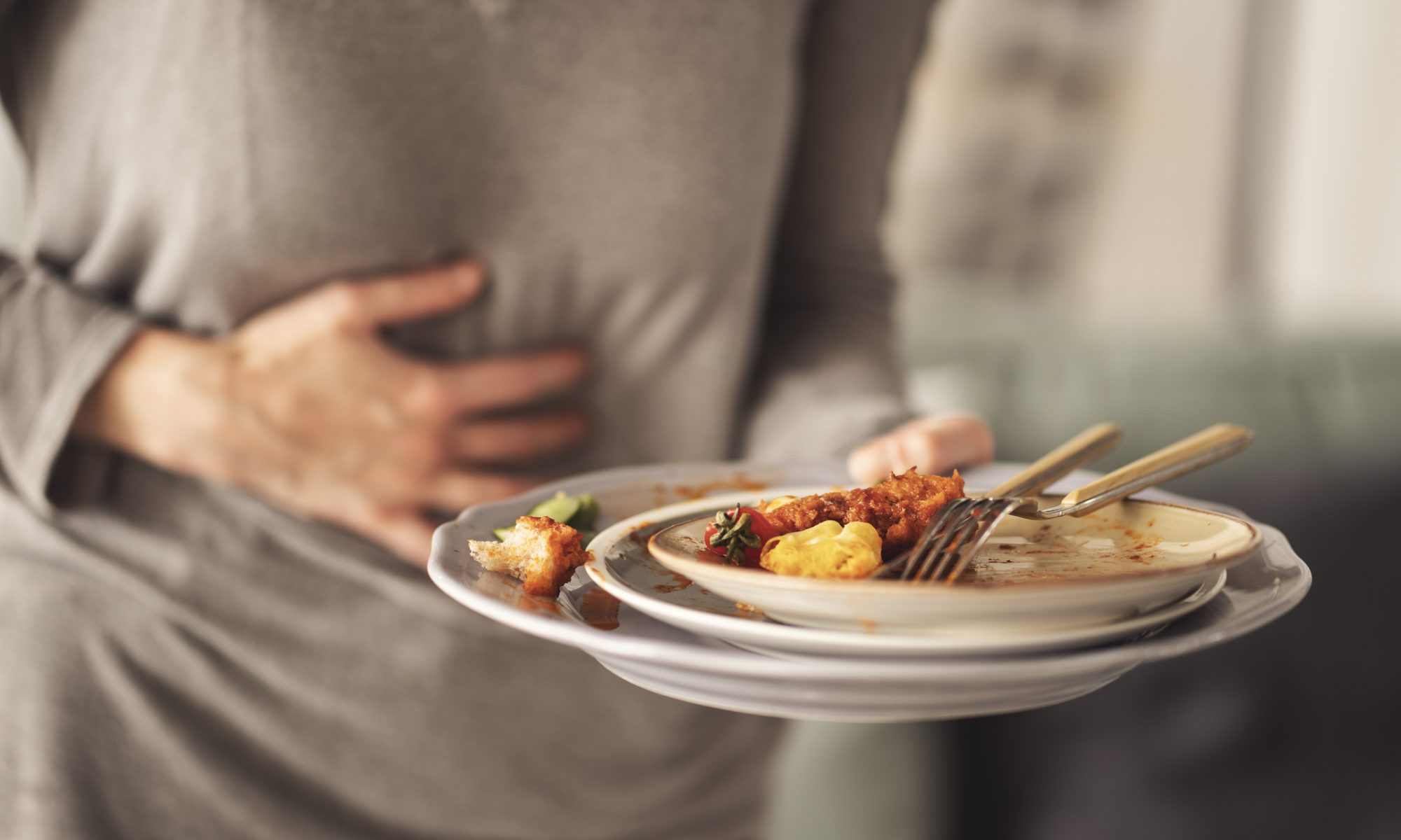 Person holding a plate of leftover food while clutching their abdomen, illustrating digestive discomfort and gastrointestinal symptoms associated with irritable bowel syndrome (IBS).