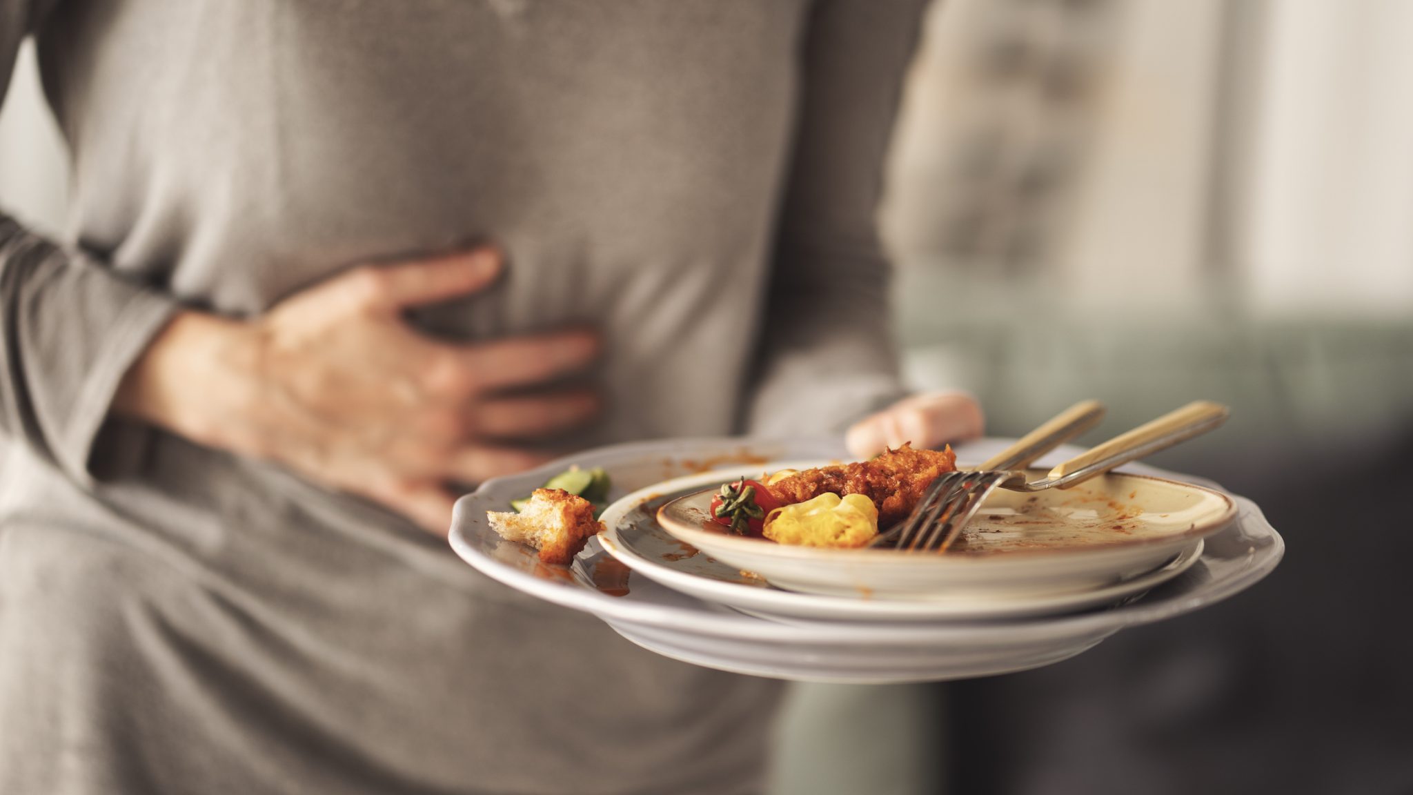 Person holding a plate of leftover food while clutching their abdomen, illustrating digestive discomfort and gastrointestinal symptoms associated with irritable bowel syndrome (IBS).