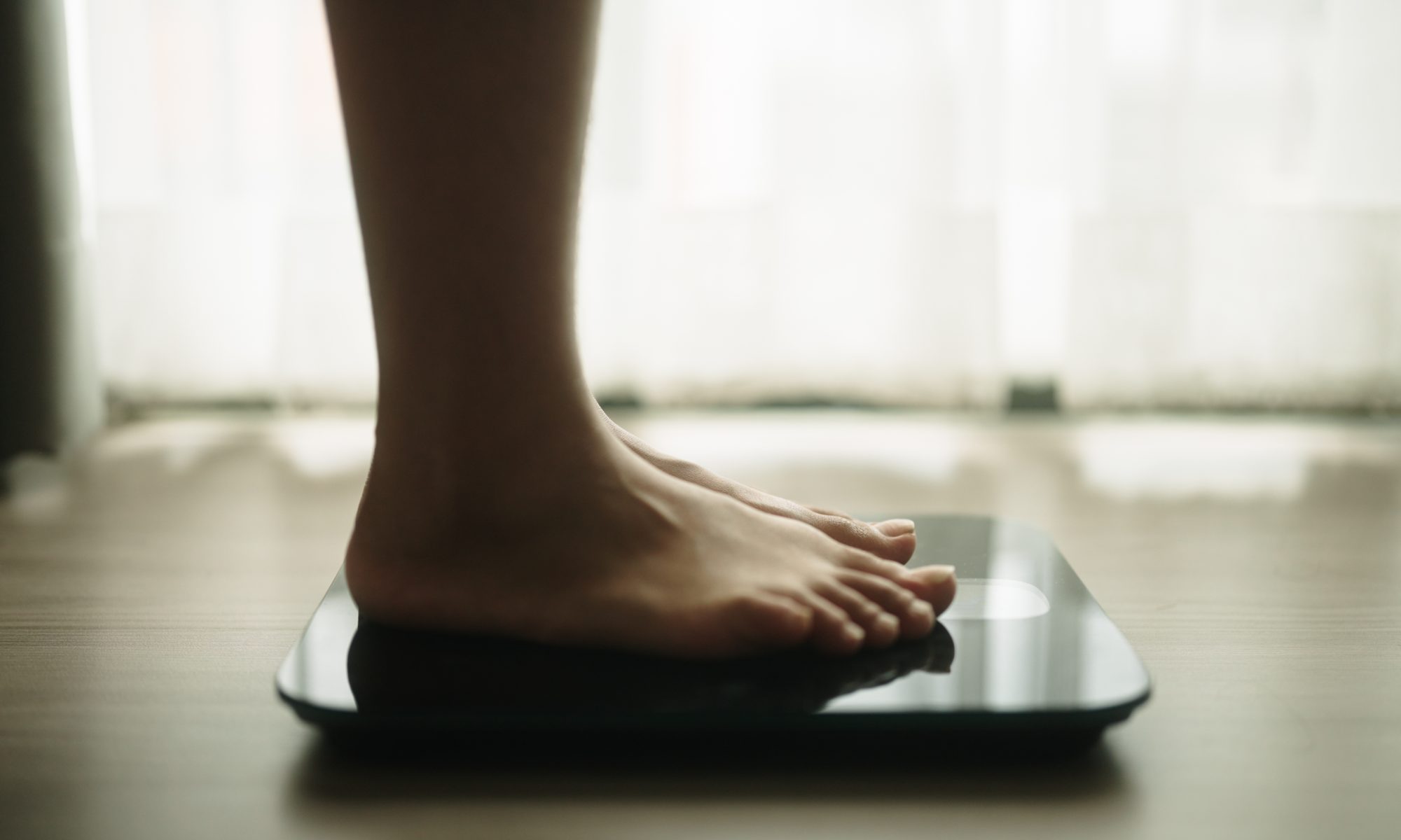 Close-up of a person standing barefoot on a digital bathroom scale, representing weight management and treatment for hypothalamic obesity.