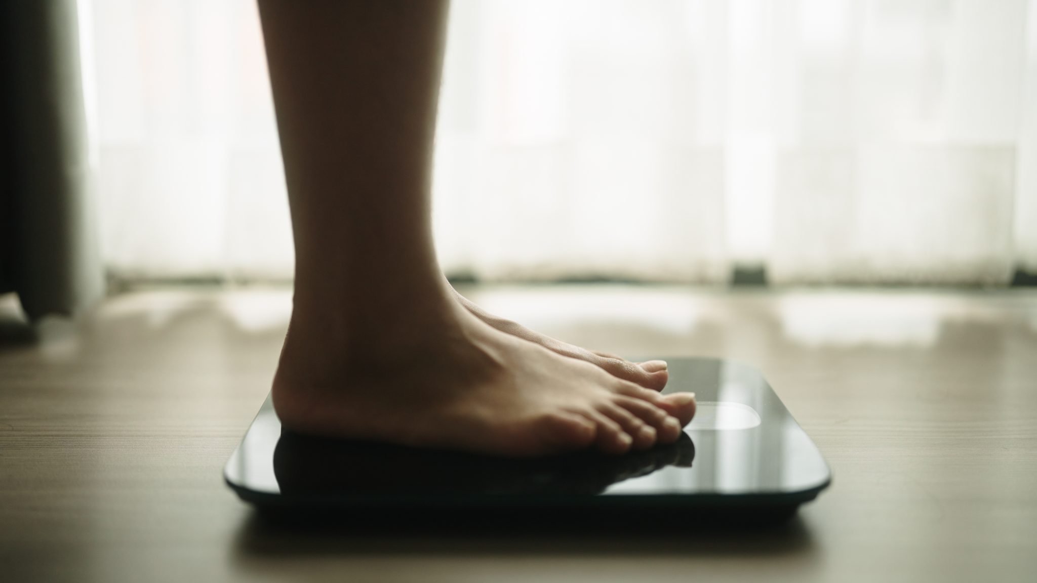 Close-up of a person standing barefoot on a digital bathroom scale, representing weight management and treatment for hypothalamic obesity.