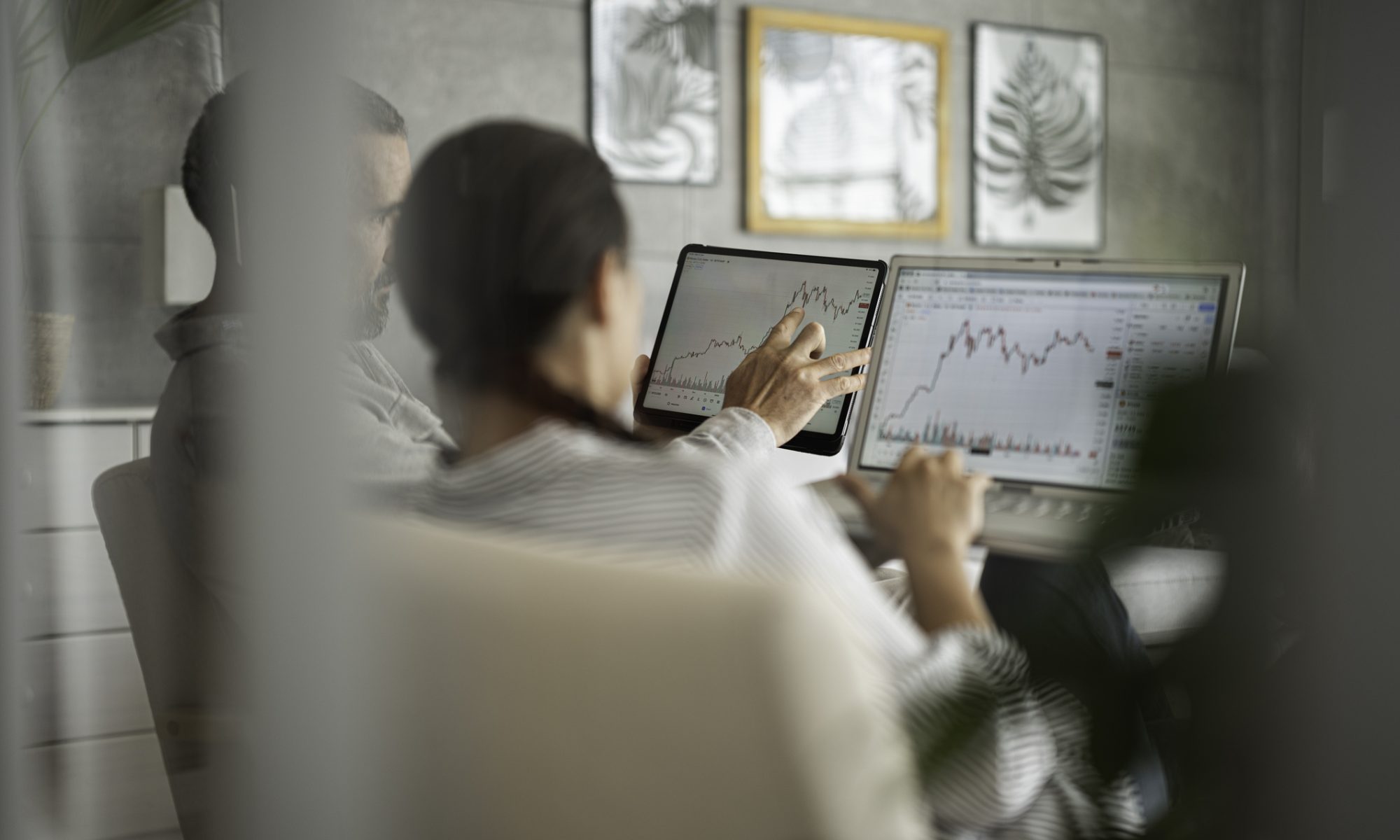 Two investors analyzing stock market charts on a tablet and laptop, illustrating midday trading activity and market movements across oil and gas, fintech and biotech stocks.