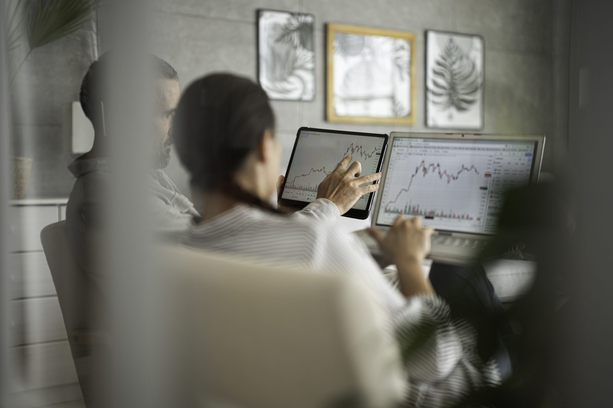 Two investors analyzing stock market charts on a tablet and laptop, illustrating midday trading activity and market movements across oil and gas, fintech and biotech stocks.