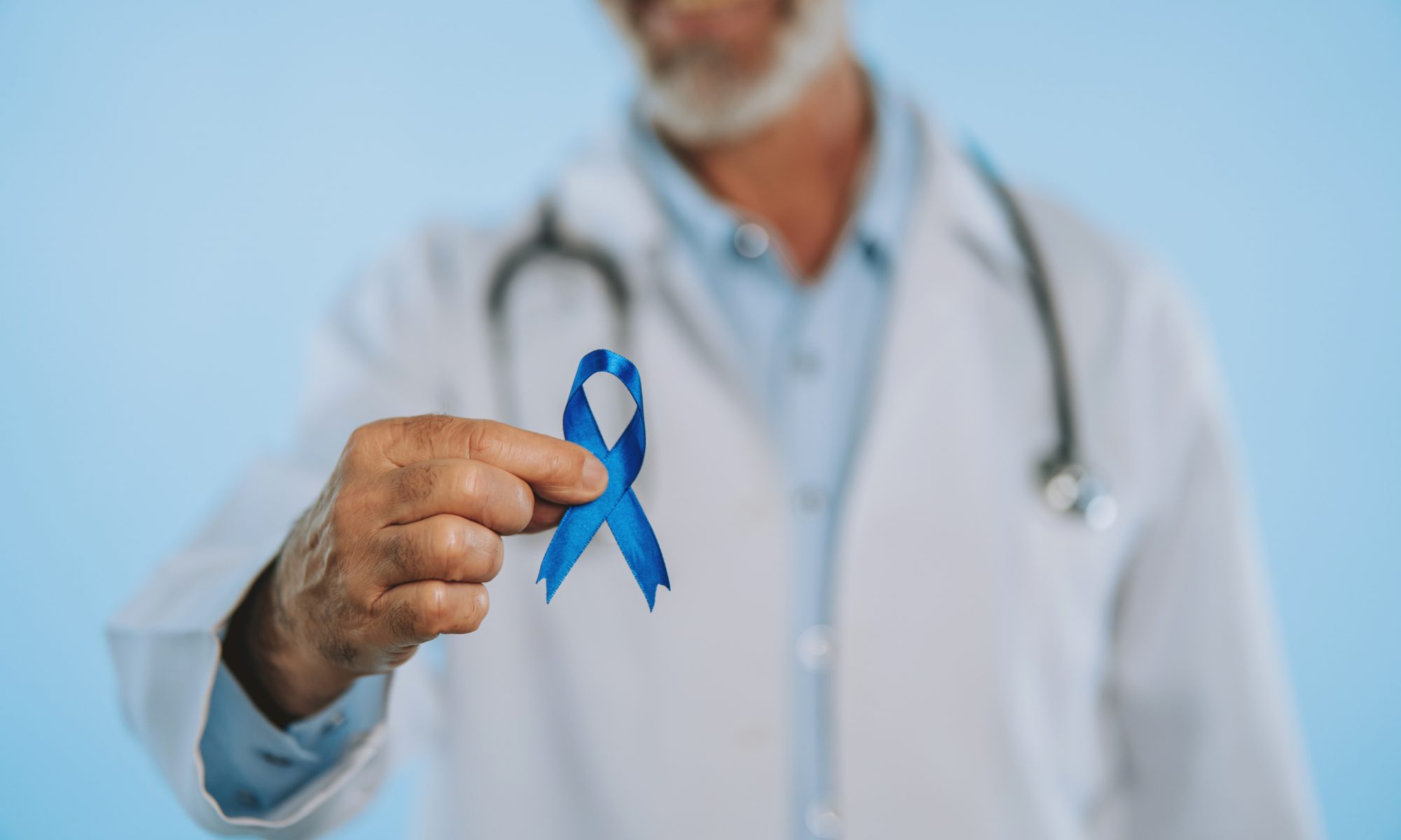 Medical professional wearing a white coat and stethoscope holds a blue prostate cancer awareness ribbon, symbolizing advances in prostate cancer treatment and research.