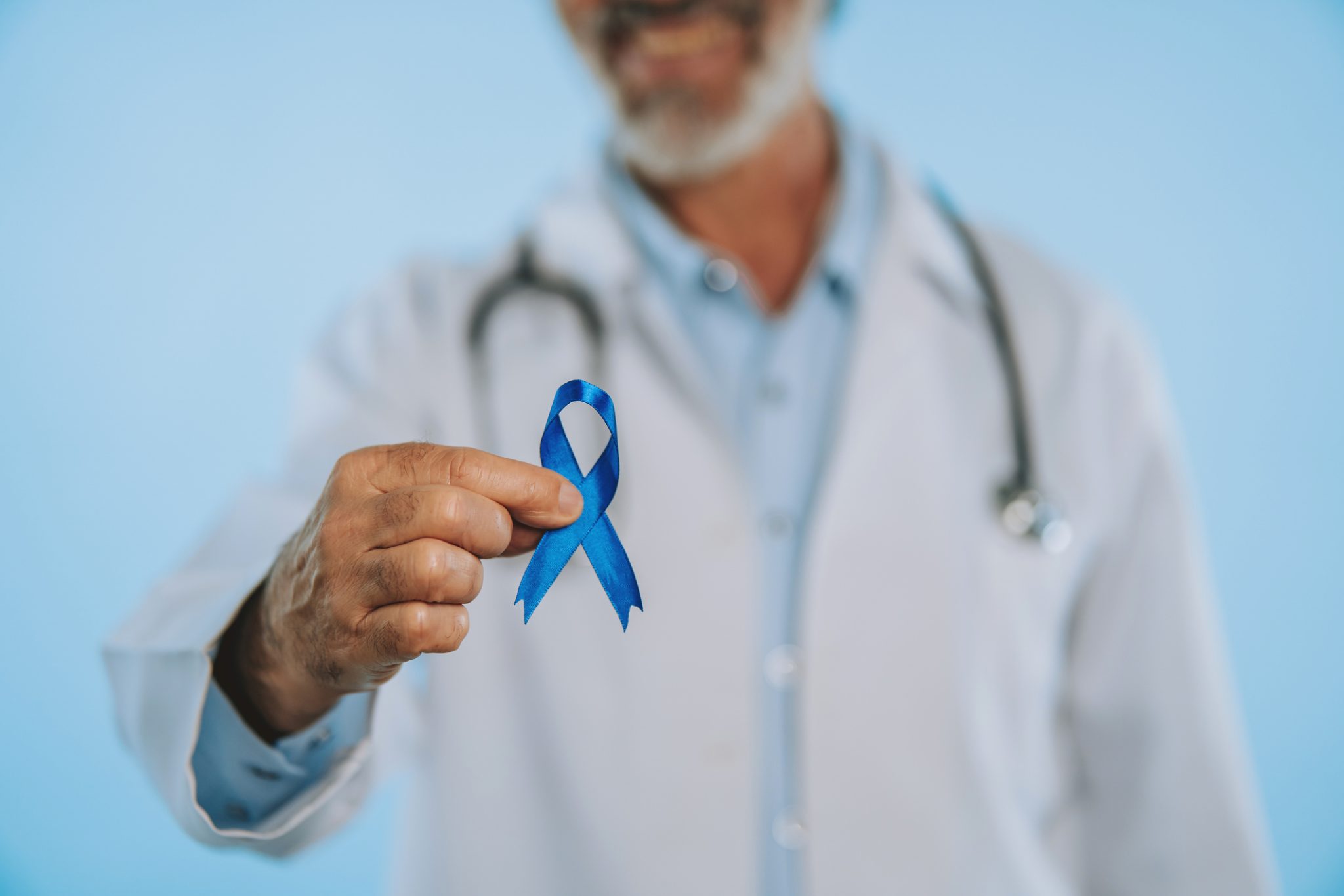 Medical professional wearing a white coat and stethoscope holds a blue prostate cancer awareness ribbon, symbolizing advances in prostate cancer treatment and research.