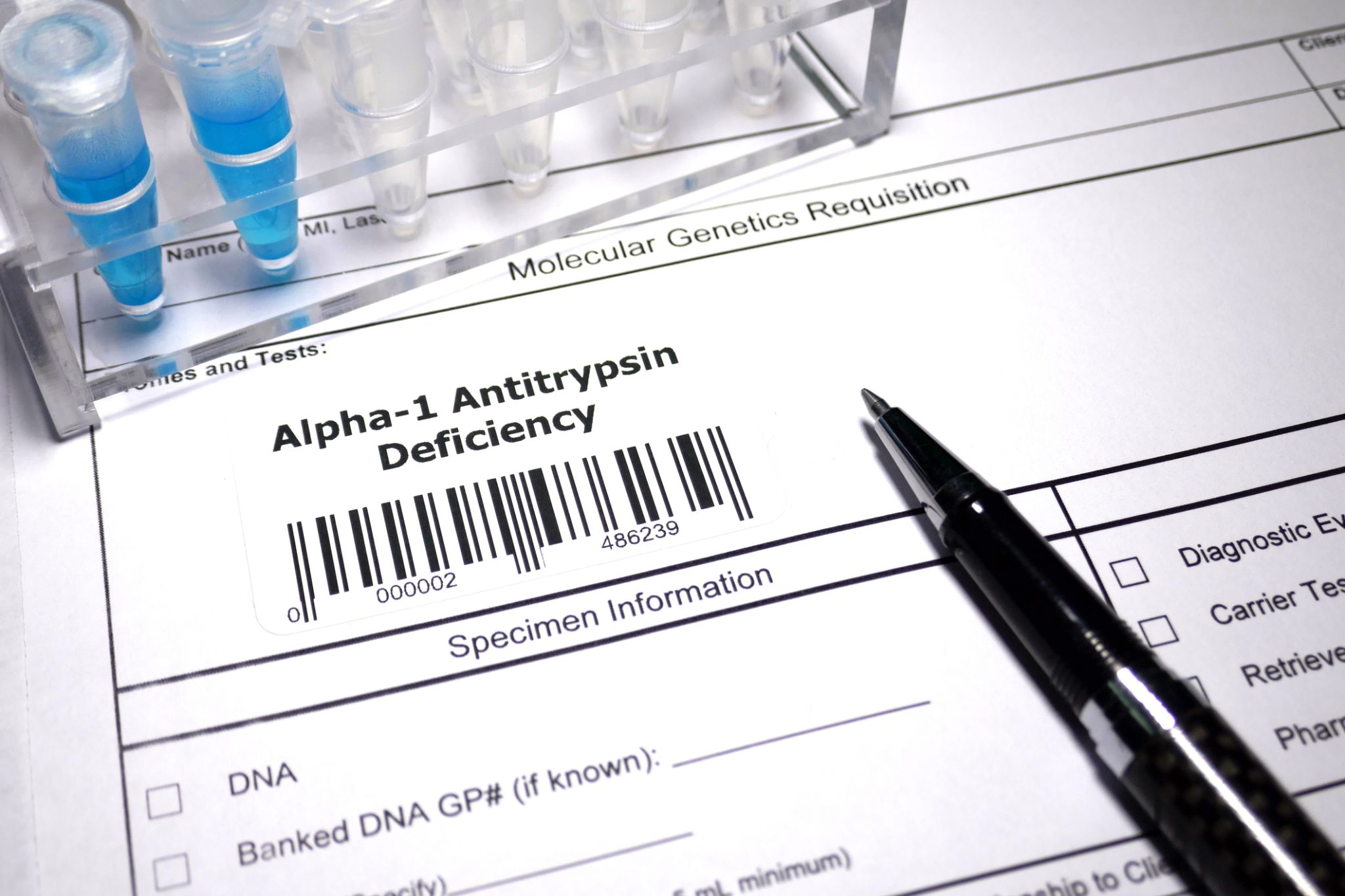 Close-up of a molecular genetics testing form labeled Alpha-1 Antitrypsin Deficiency, alongside laboratory sample tubes and a pen, illustrating genetic research and testing for AATD.