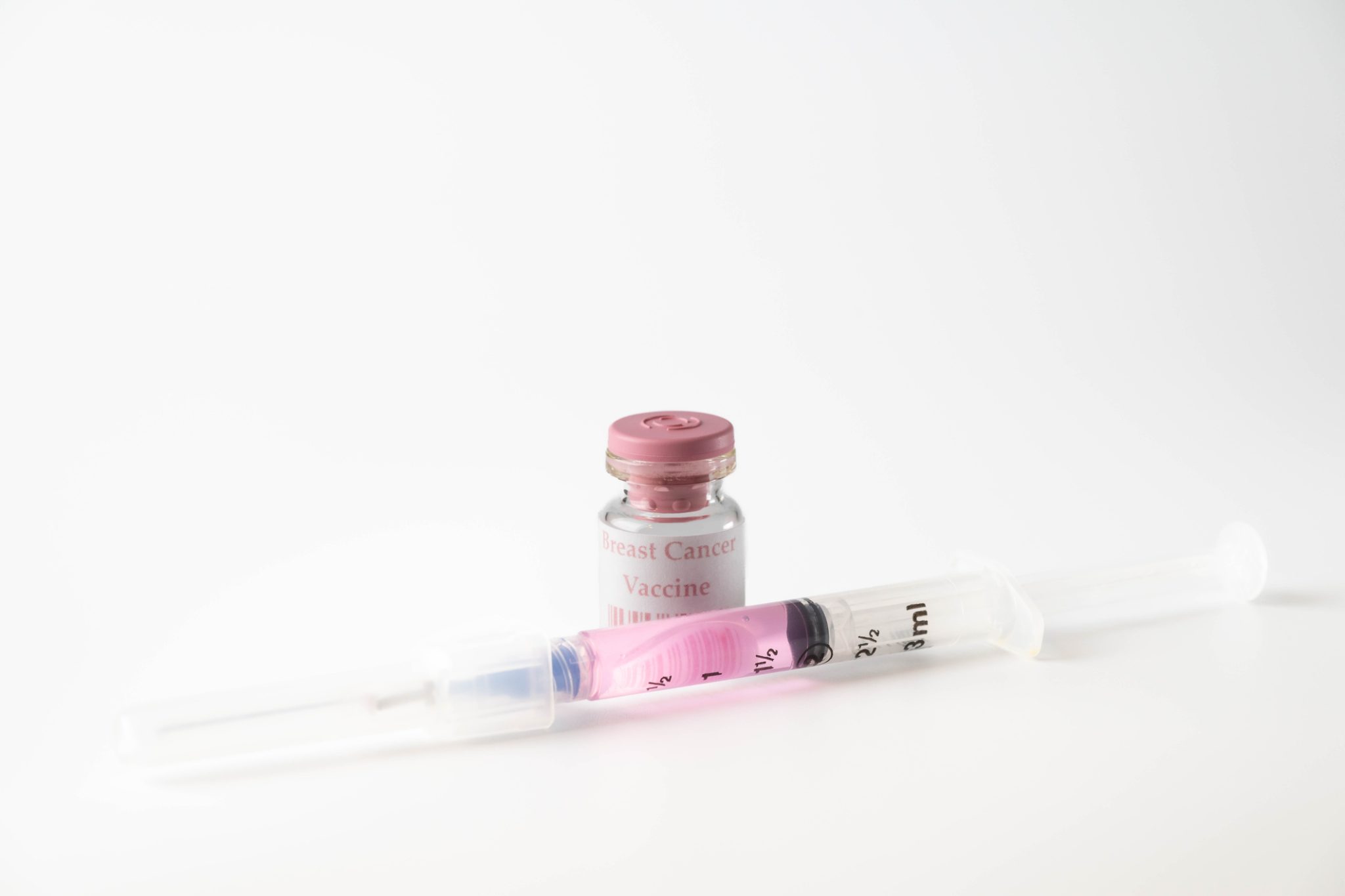 Small vial labeled "Breast Cancer Vaccine" with a syringe containing pink liquid against a clean white background, representing breast cancer immunotherapy research.